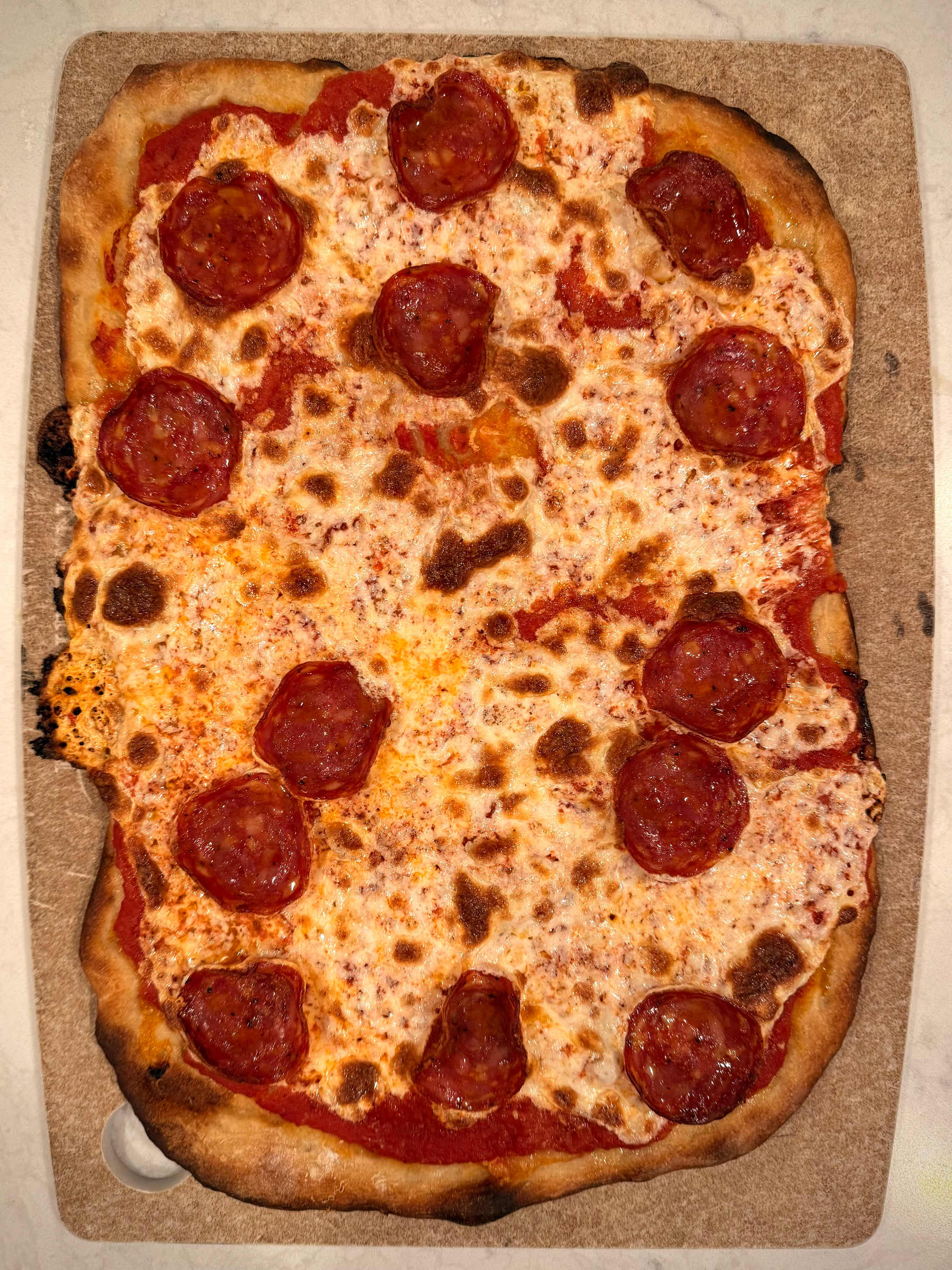 A rectangular pizza topped with pepperoni and melted cheese is displayed on a wooden surface.
