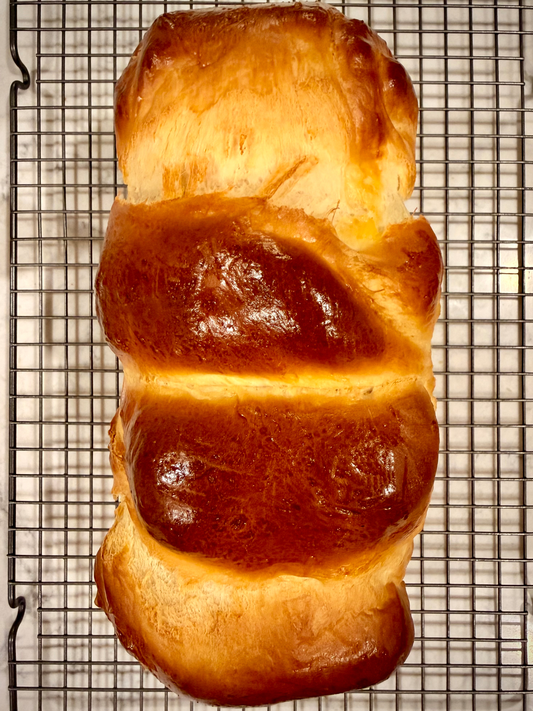A freshly baked loaf of bread with a golden brown crust is cooling on a wire rack.