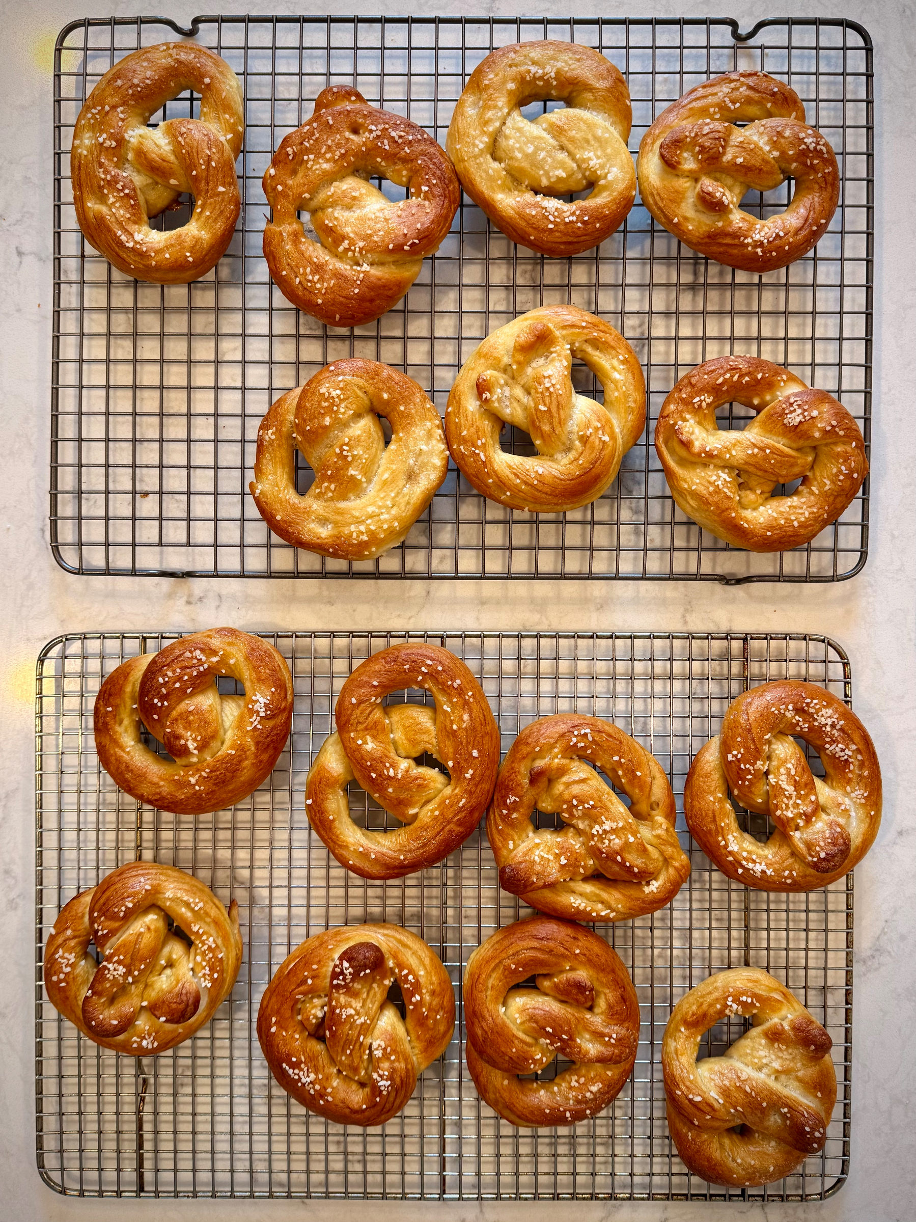 Several freshly baked pretzels are cooling on two wire racks.