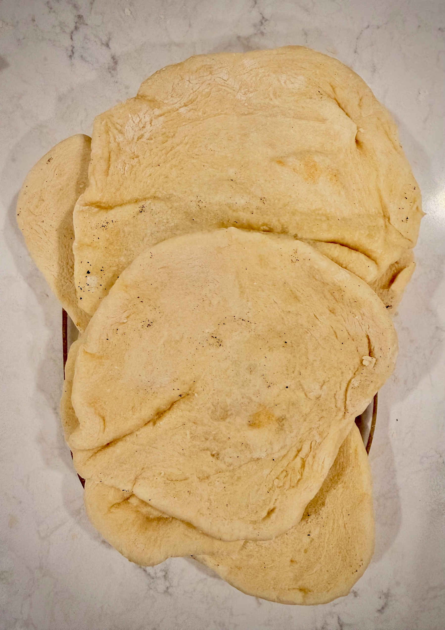Several pieces of flatbread are stacked on a white marble surface.