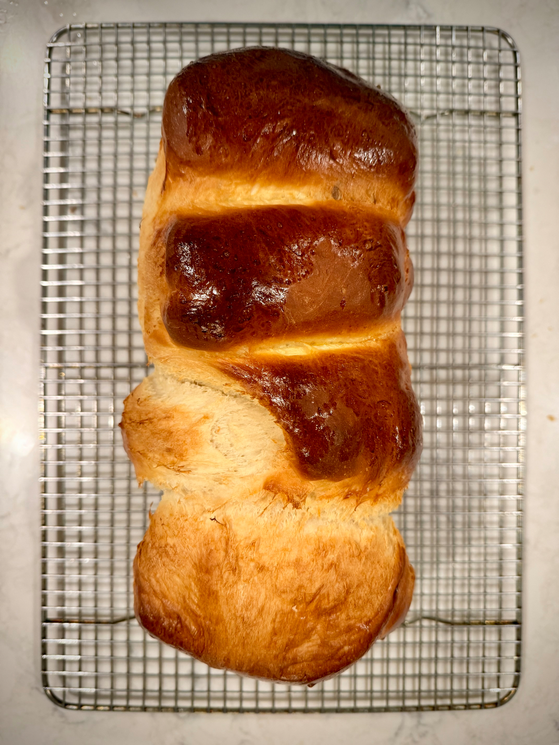 A freshly baked loaf of bread with a glossy, golden-brown crust rests on a cooling rack.