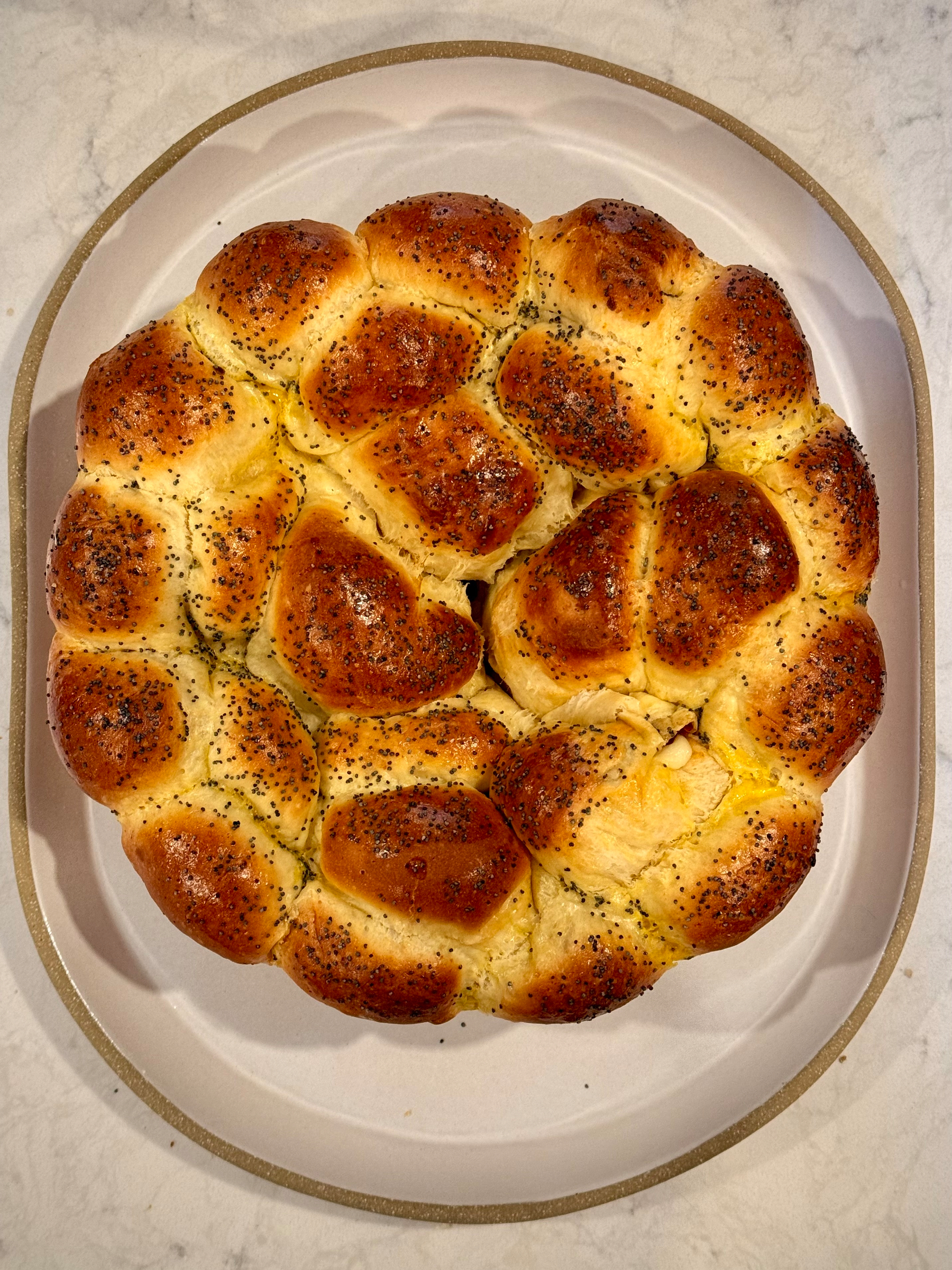 A freshly baked, round bread topped with poppy seeds is placed on a white plate.