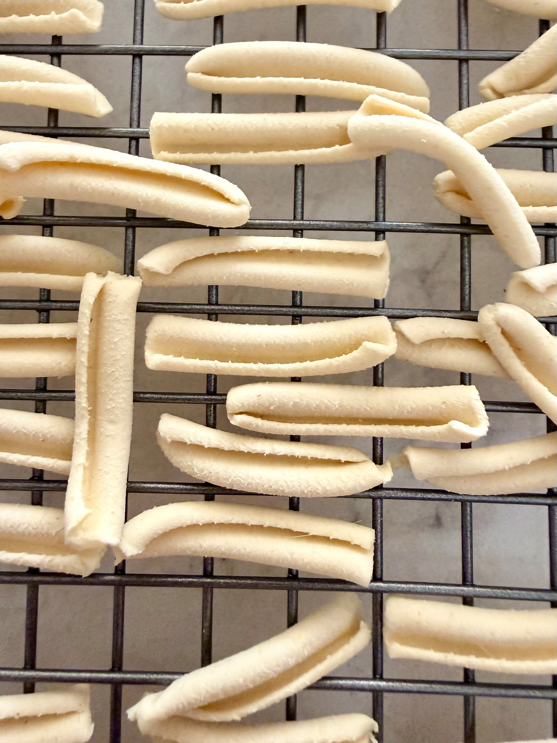 Several uncooked cavatelli pasta pieces are arranged on a cooling rack.