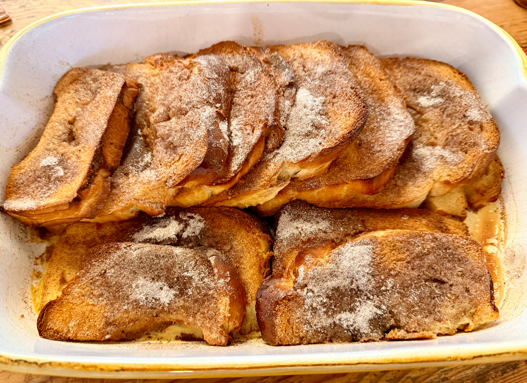 Slices of baked French toast are arranged in a dish, topped with a sprinkle of sugar.