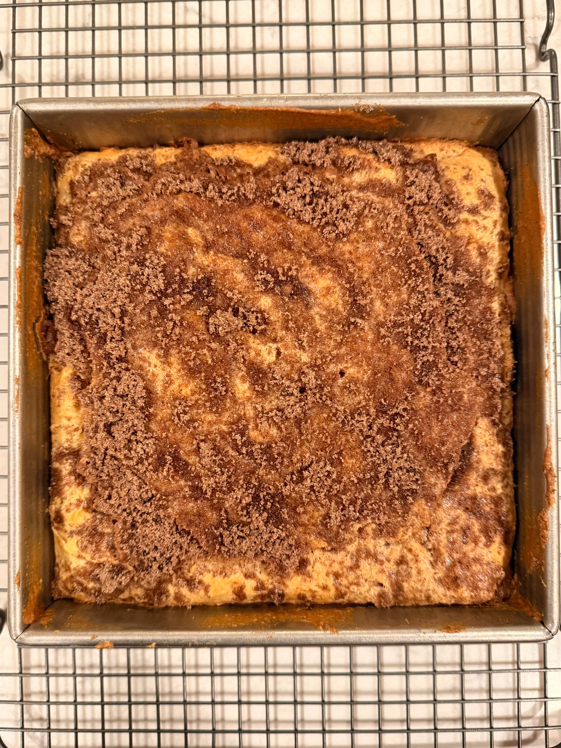A freshly baked coffee cake topped with a layer of crumbly cinnamon-brown sugar is cooling on a wire rack.