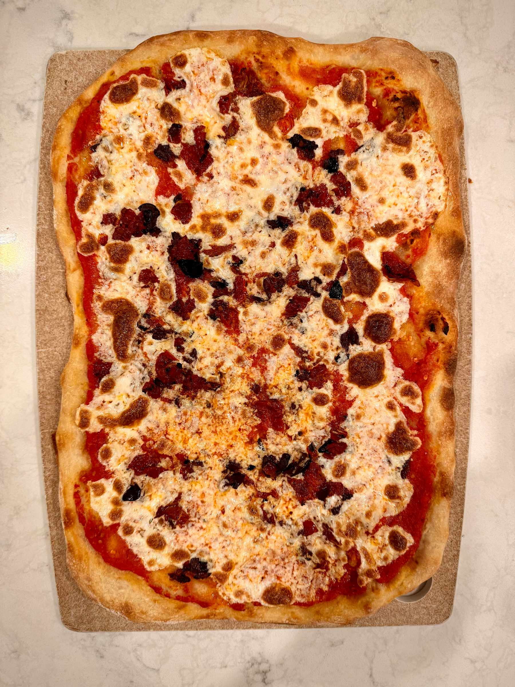A rectangular pizza topped with melted cheese and olives is placed on a wooden board.