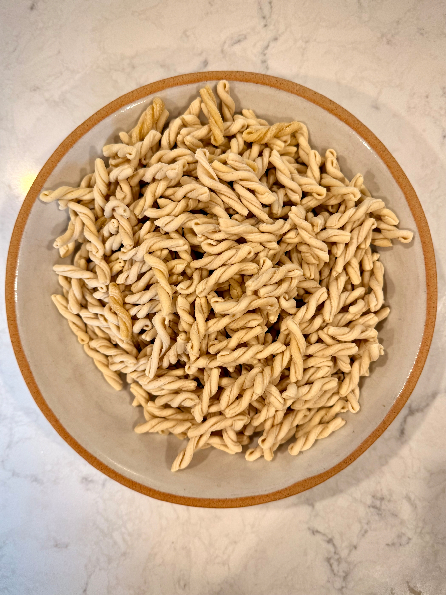 A bowl filled with twisted pasta pieces sits on a marble surface.