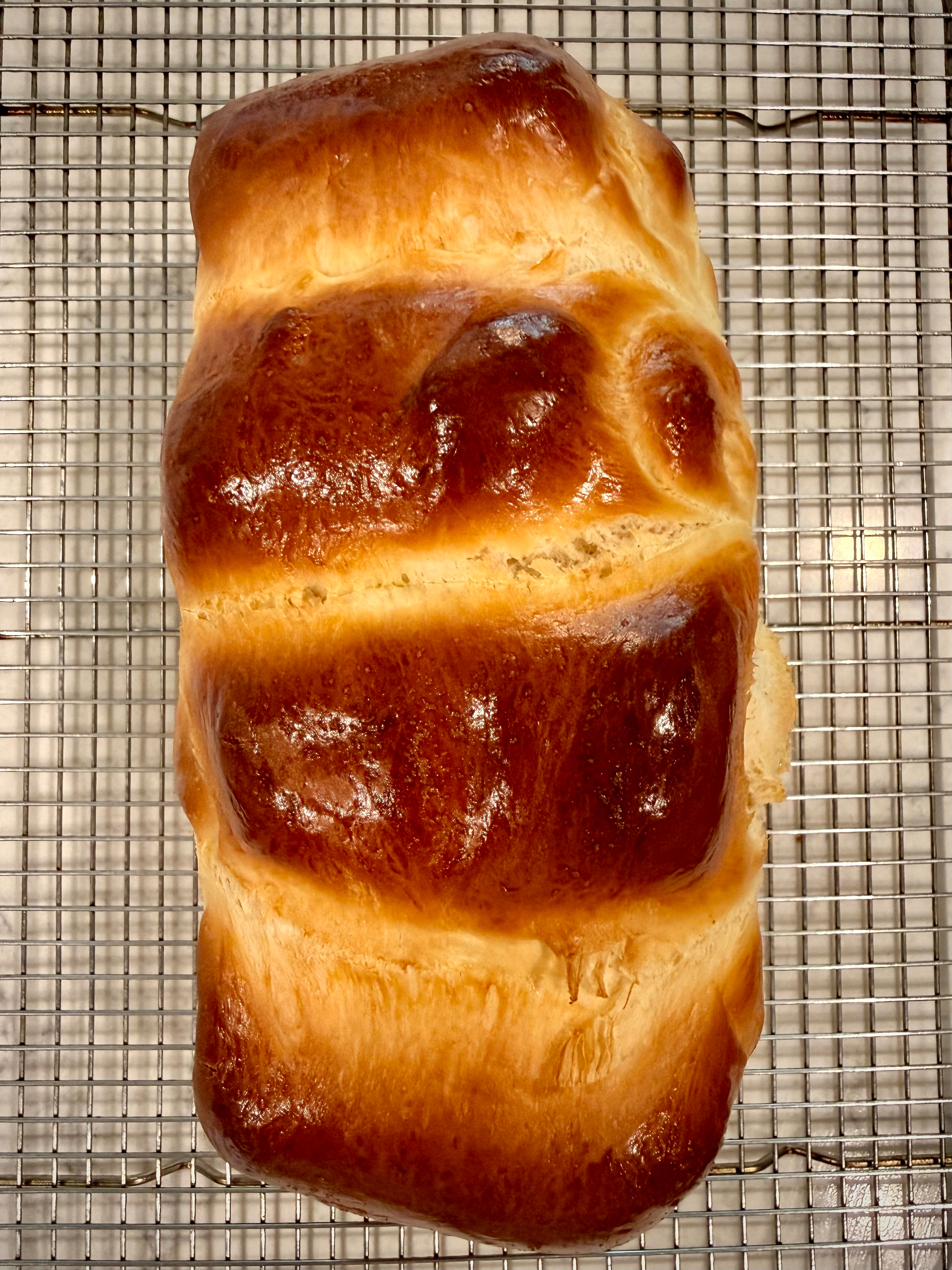 A freshly baked loaf of golden brown bread rests on a cooling rack.
