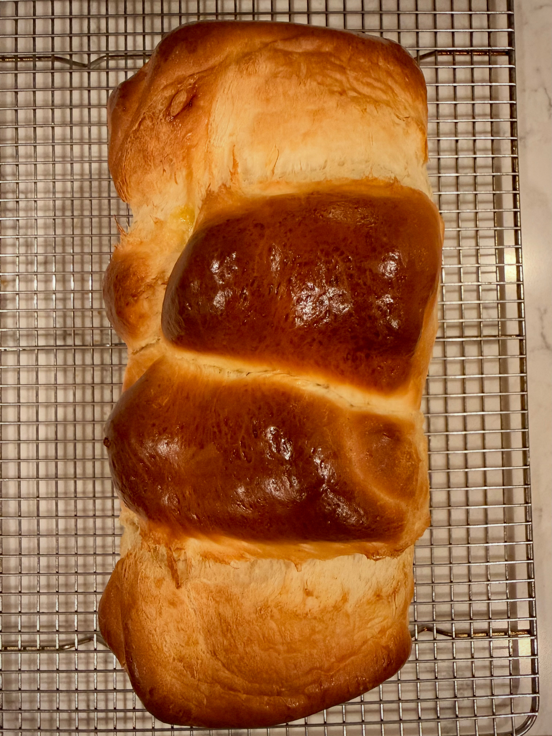 A freshly baked loaf of bread with a golden-brown crust is cooling on a wire rack.
