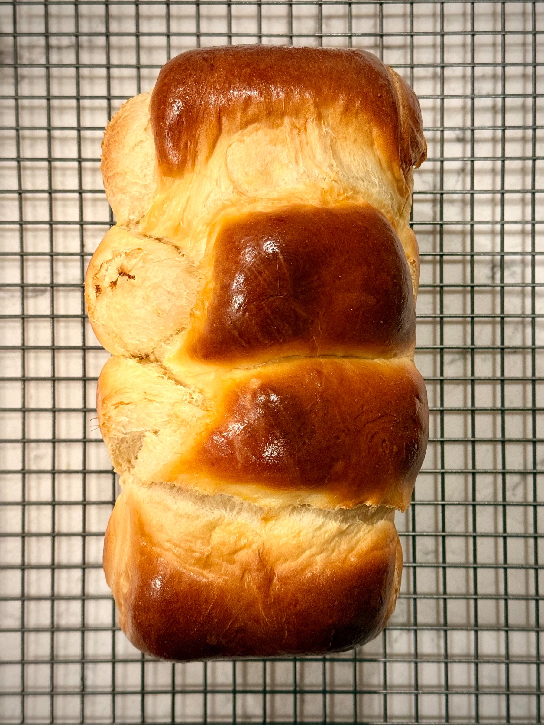 A loaf of braided bread sits on a cooling rack, displaying a shiny, golden-brown crust.