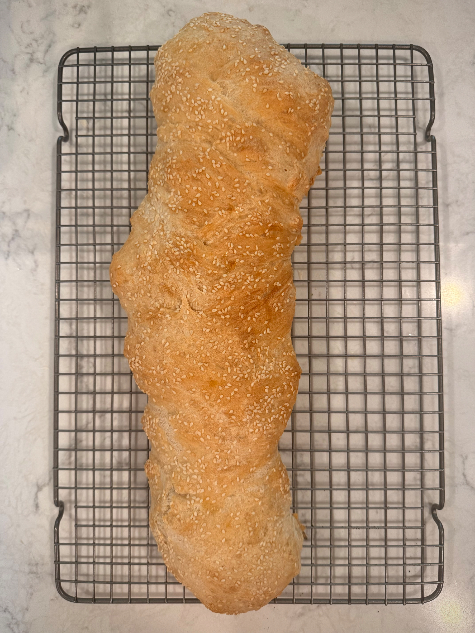 A loaf of freshly baked, sesame-seeded bread is resting on a cooling rack.