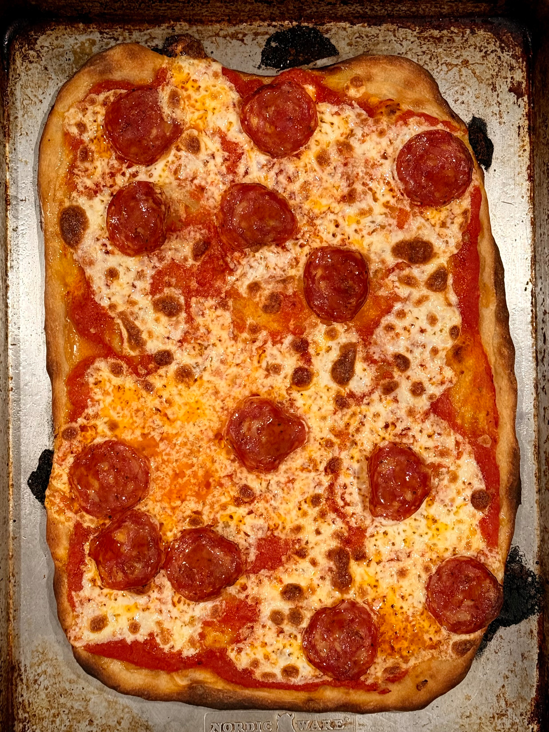 A homemade rectangular pepperoni pizza with a crispy crust is displayed on a metal baking sheet.