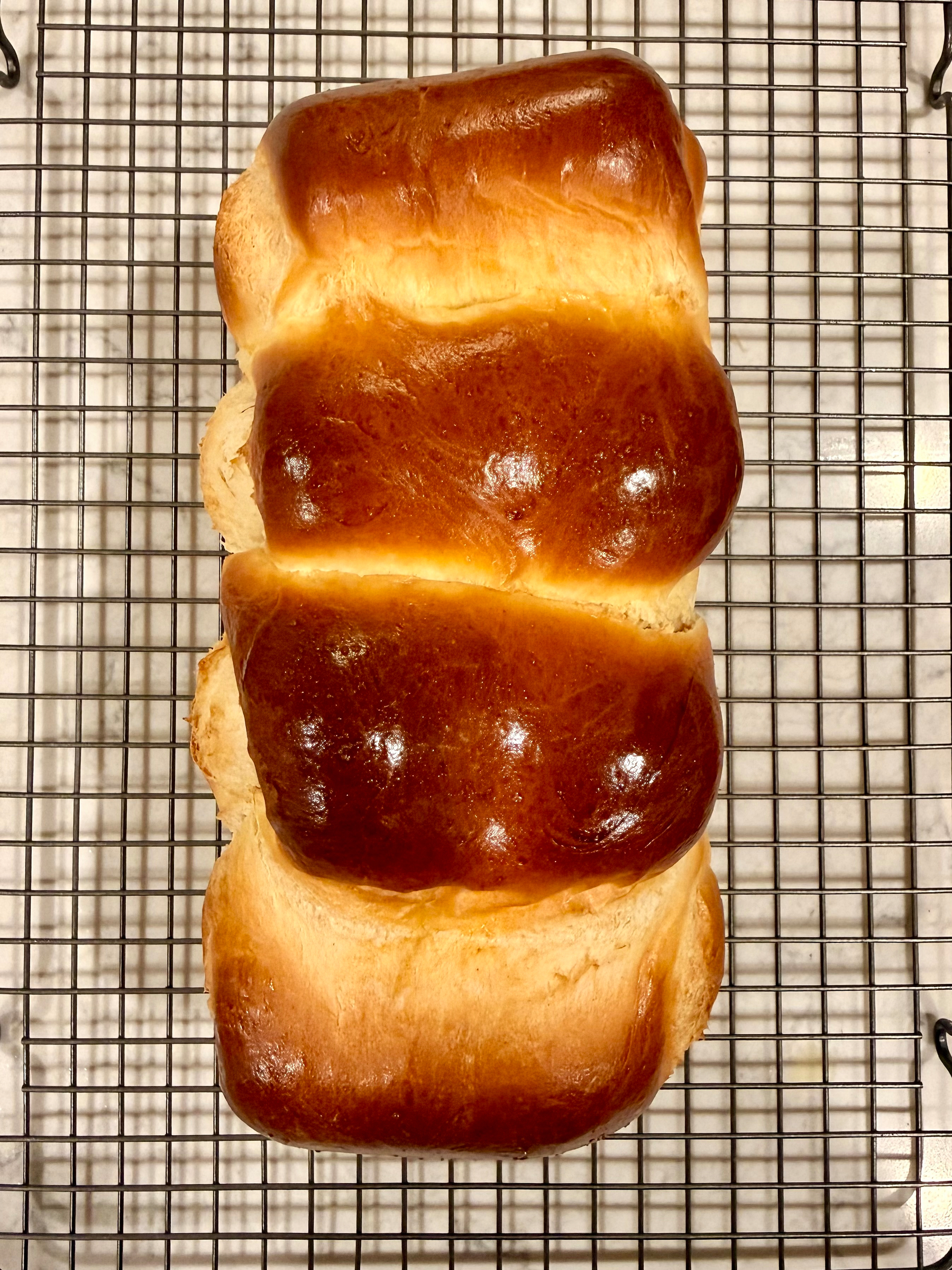A freshly baked, shiny loaf of bread is cooling on a wire rack.