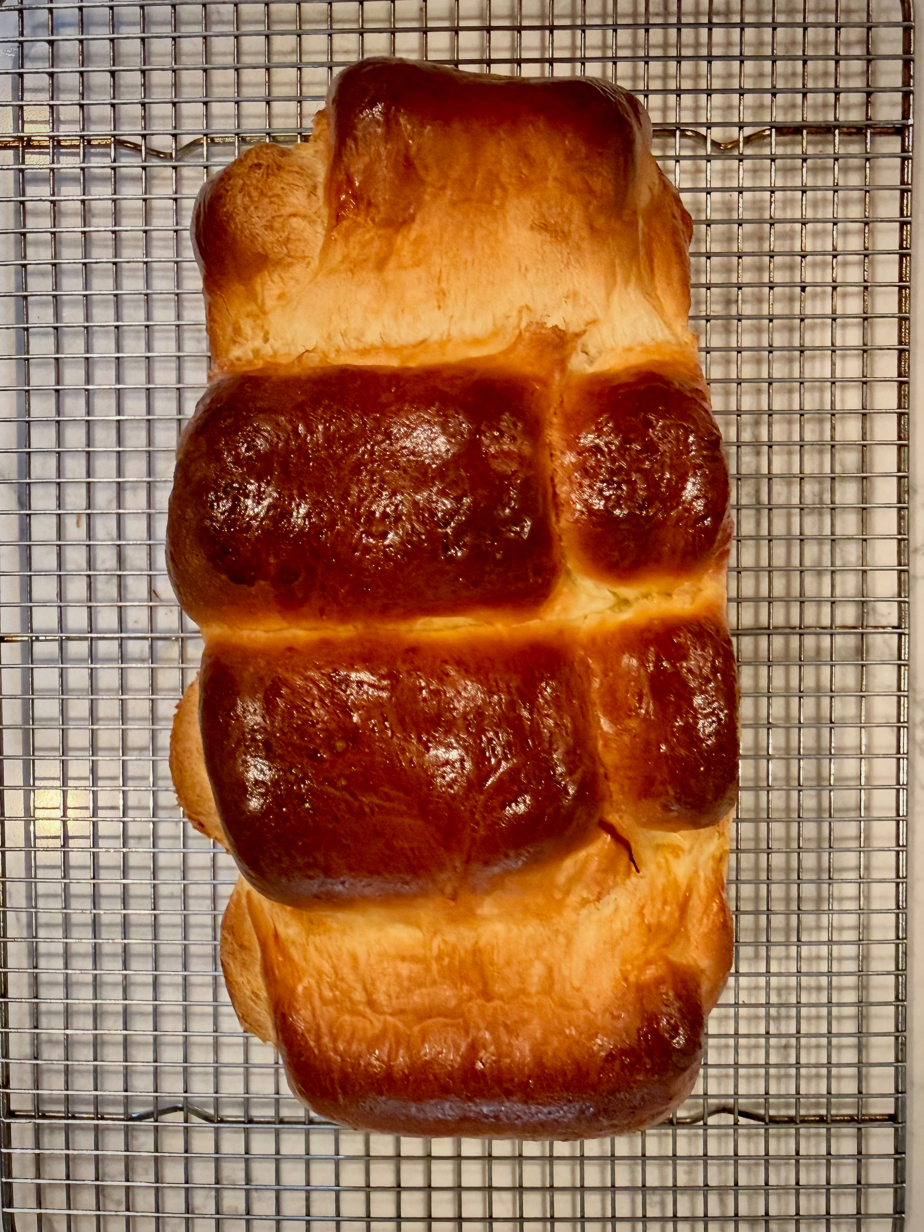 A freshly baked loaf of bread with a golden-brown crust rests on a cooling rack.