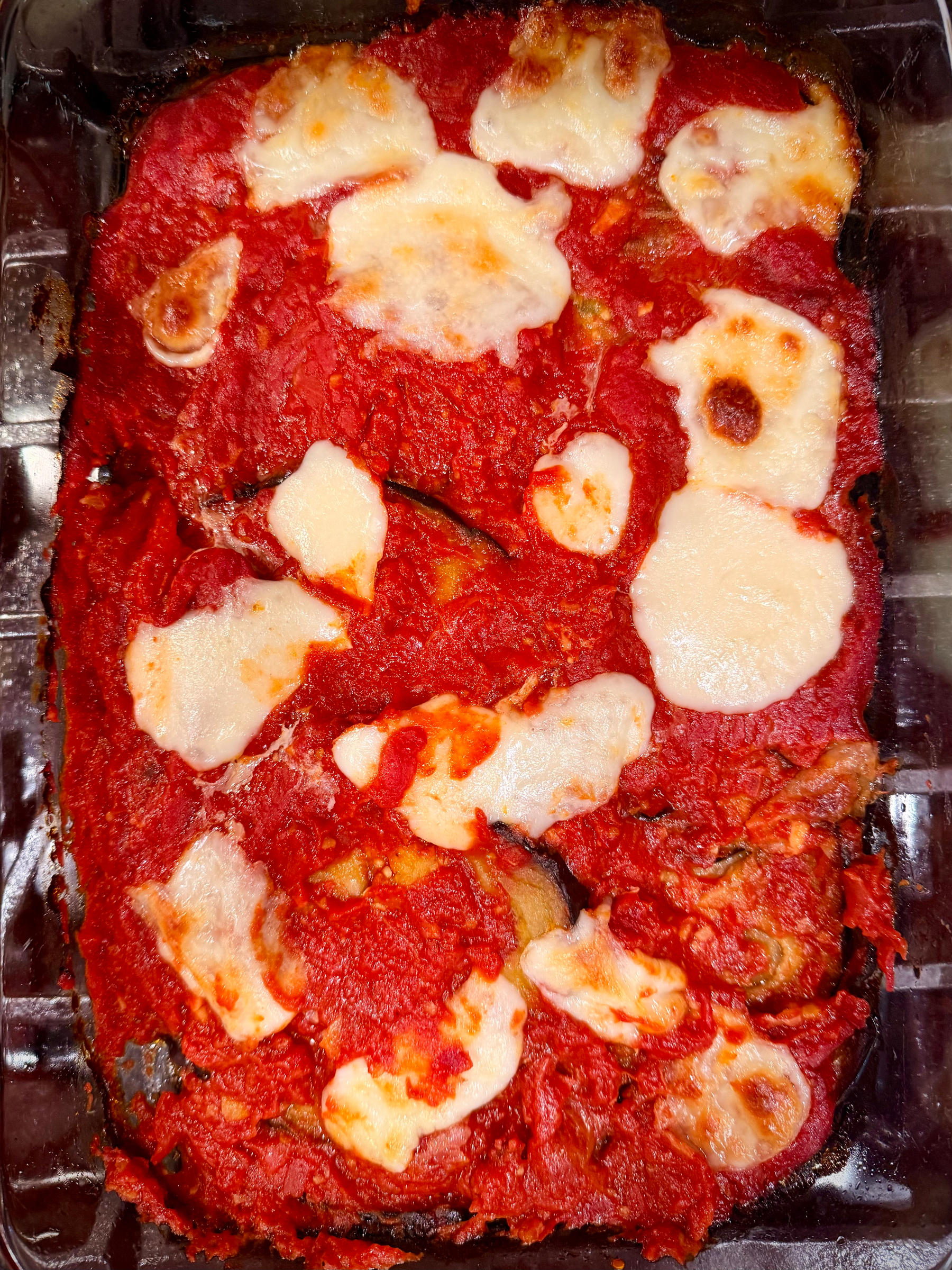 A baked dish consisting of tomato sauce and melted cheese, likely a type of lasagna or eggplant Parmesan, is displayed in a rectangular glass baking dish.