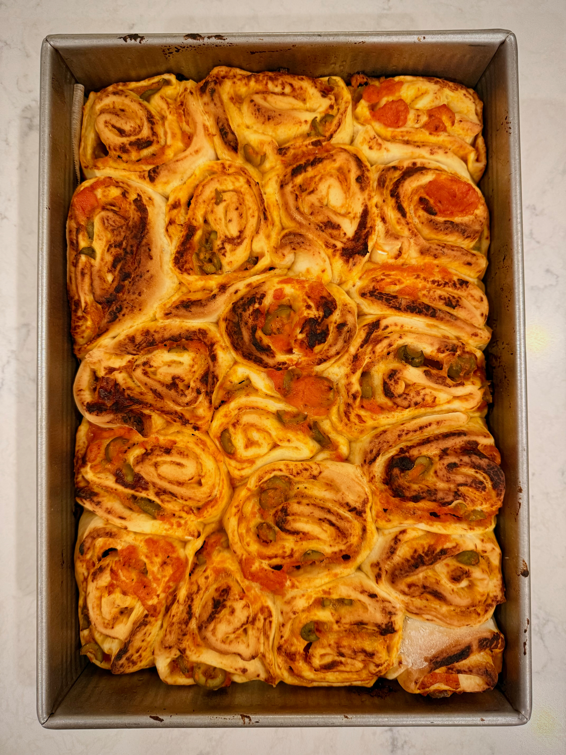 A tray filled with freshly baked, spiral-shaped rolls featuring a savory filling.