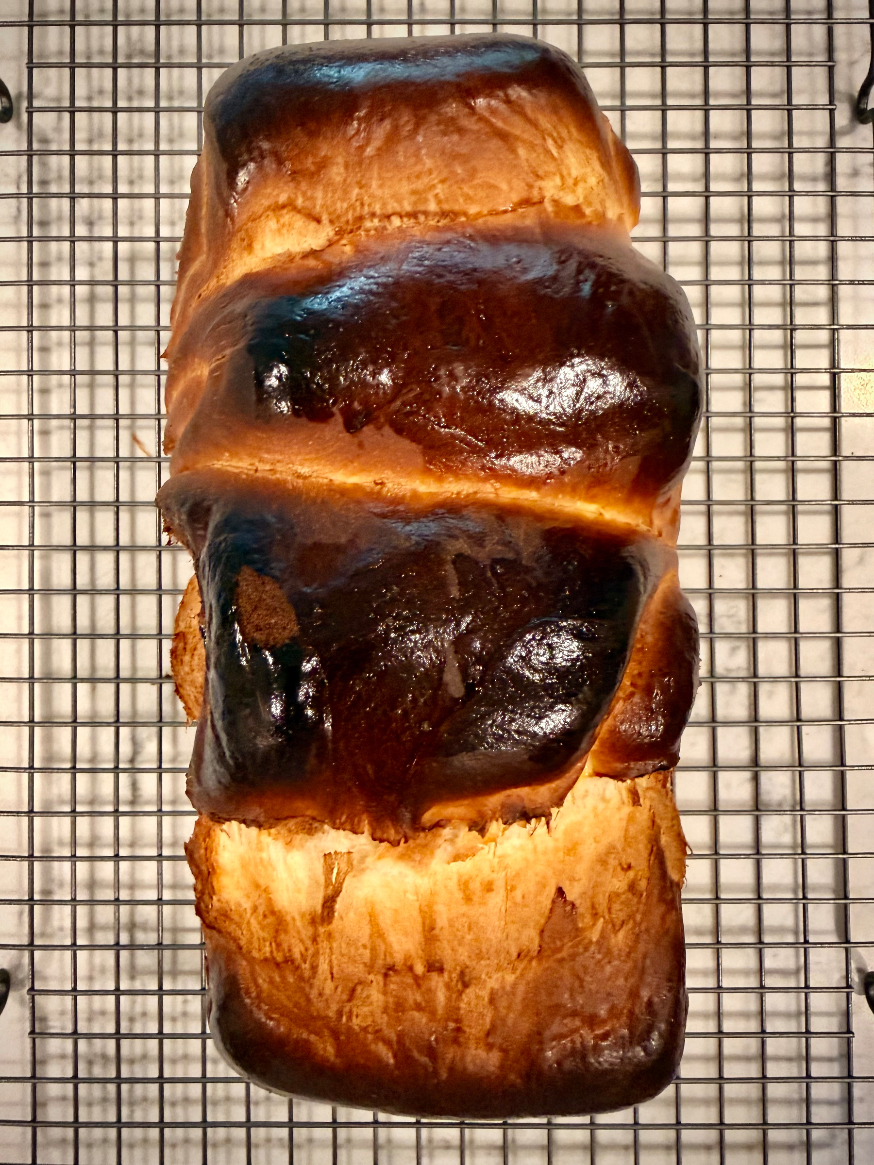 A a slightly burnt loaf of brioche bread is cooling on a wire rack