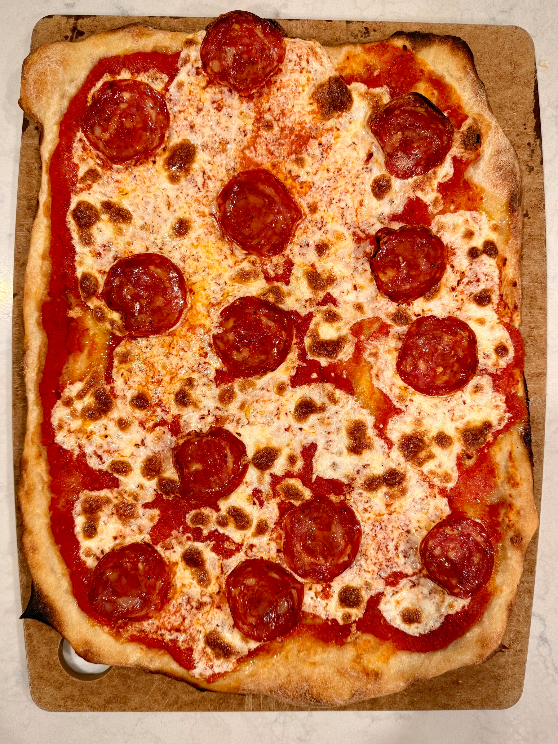 A rectangular pizza topped with pepperoni, melted cheese, and tomato sauce is placed on a baking sheet.