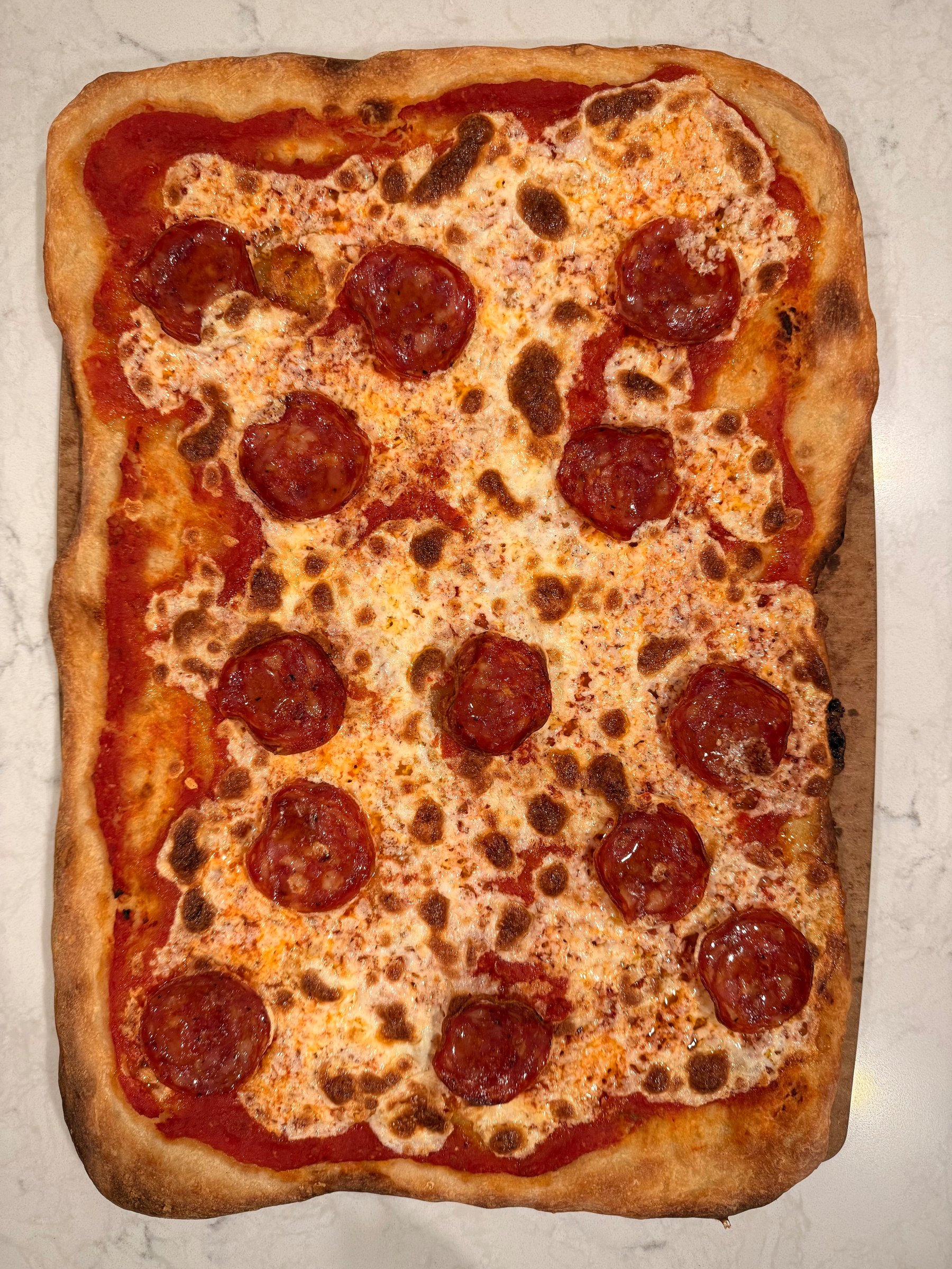 A rectangular pizza with crispy edges is topped with melted cheese and pepperoni slices on a white surface.