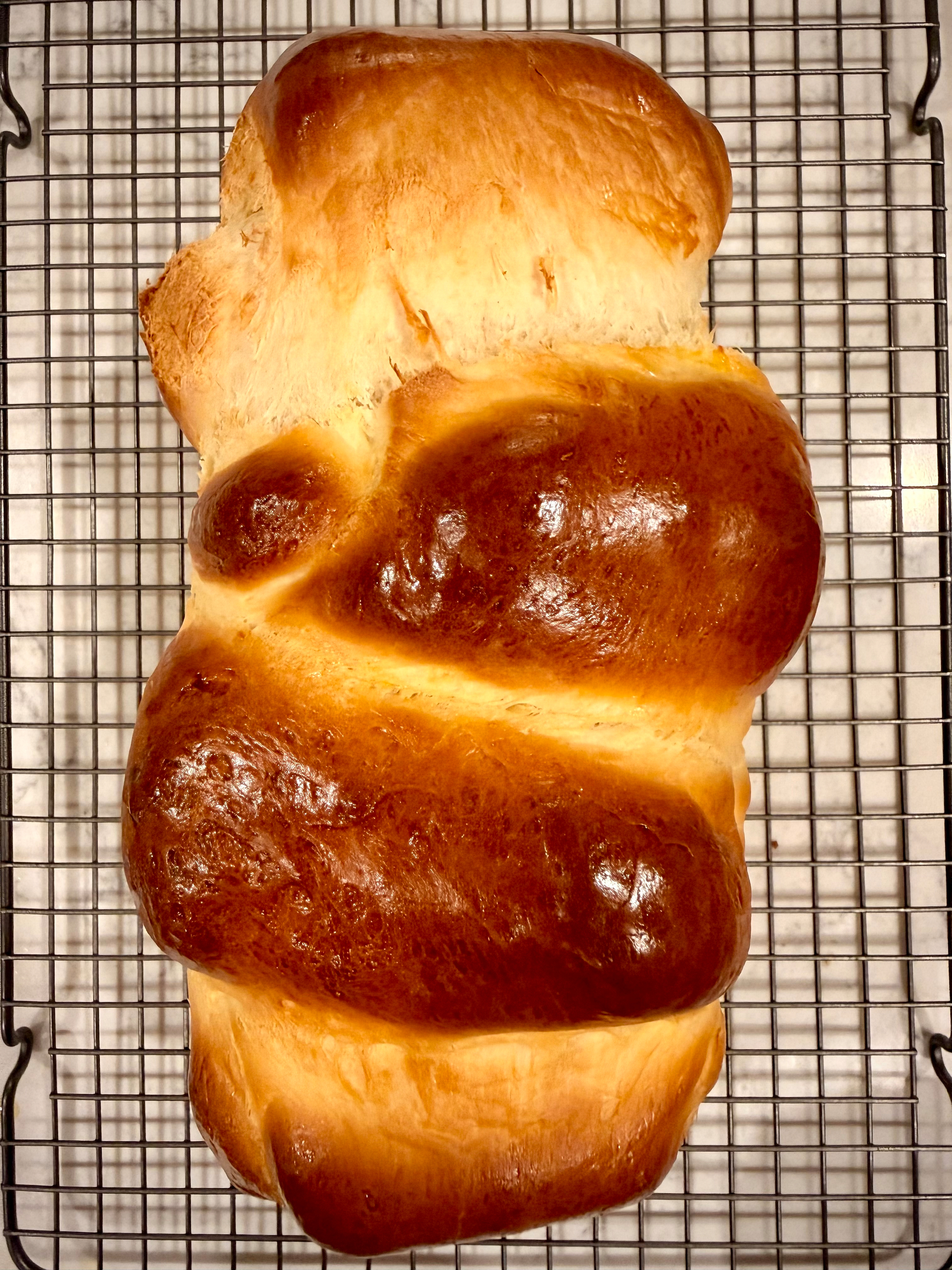 A freshly baked loaf of braided bread is cooling on a wire rack.
