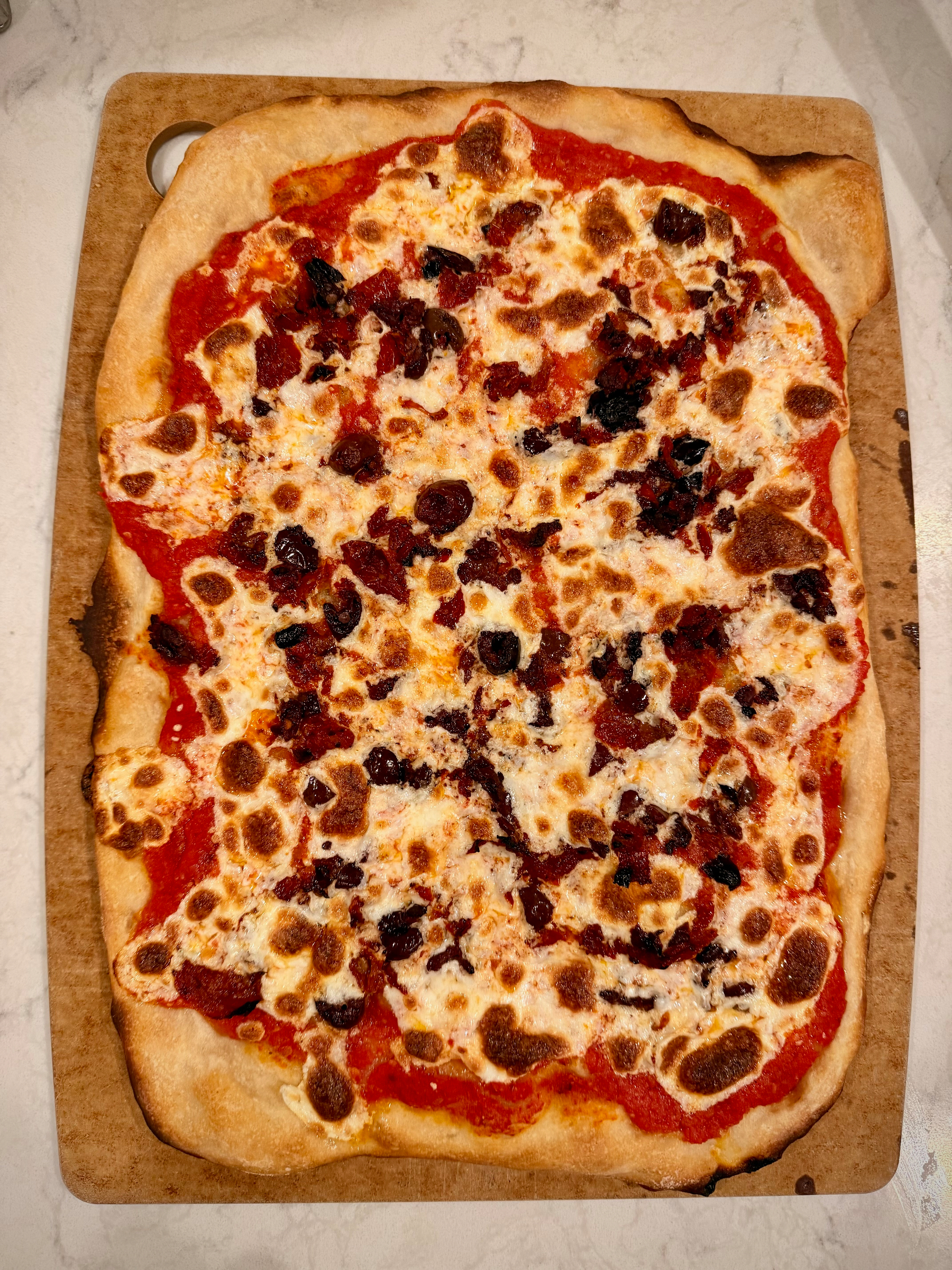 A rectangular pizza with a crispy crust is topped with melted cheese, olives, and a tomato-based sauce.