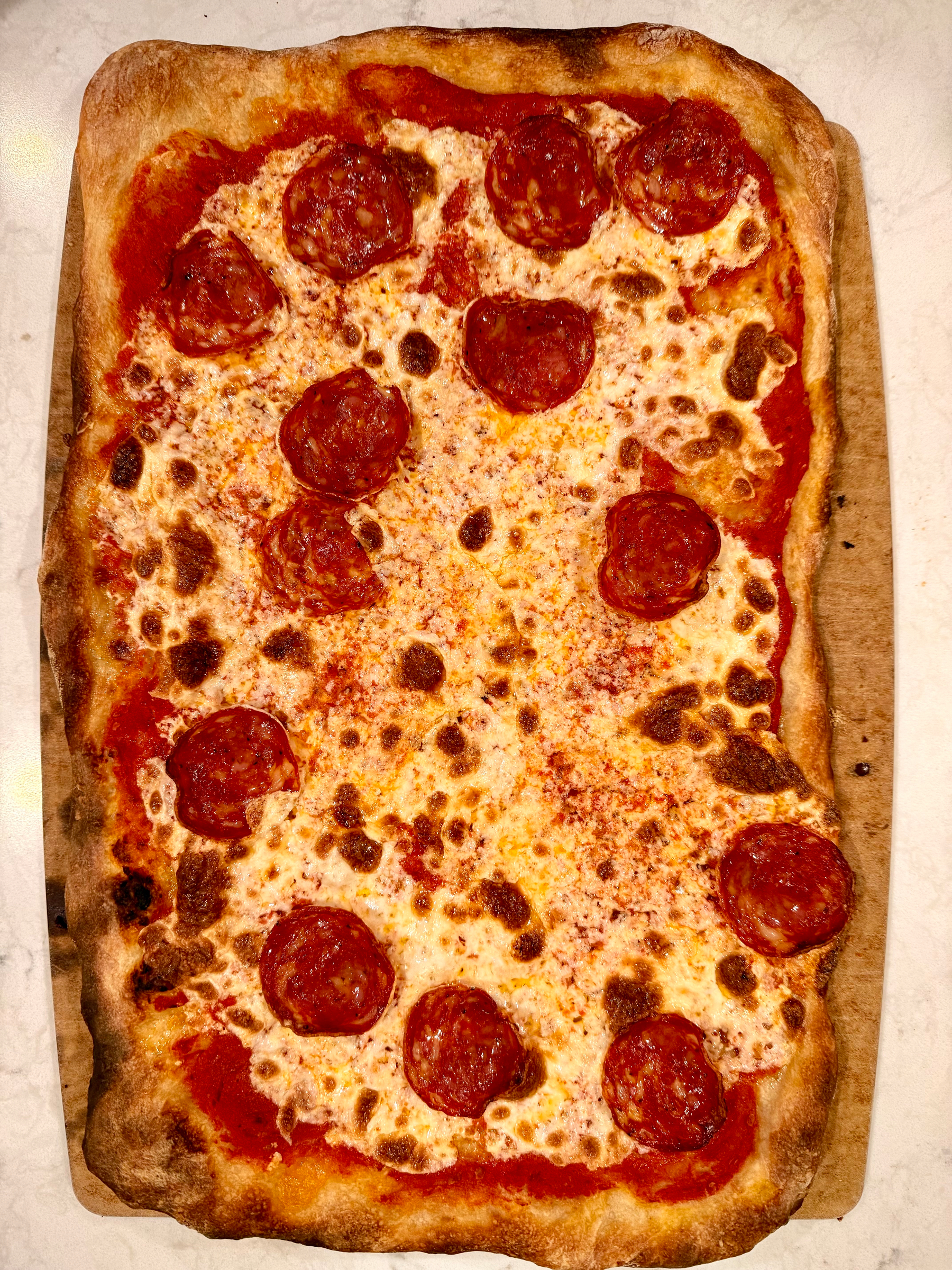 A rectangular pepperoni pizza on a wooden board with a bubbly, golden-brown crust.