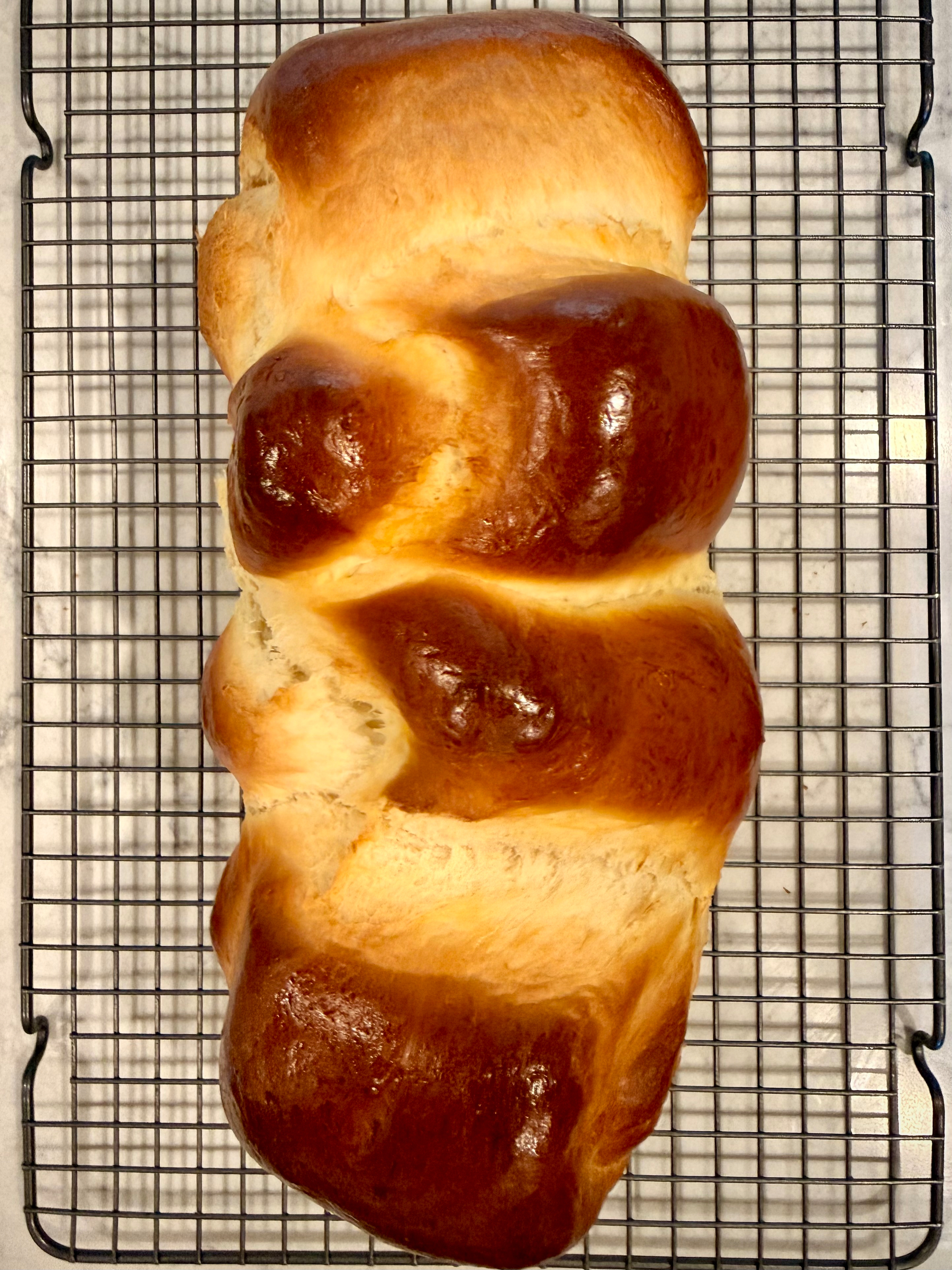 A freshly baked loaf of braided bread with a golden-brown crust is cooling on a wire rack.