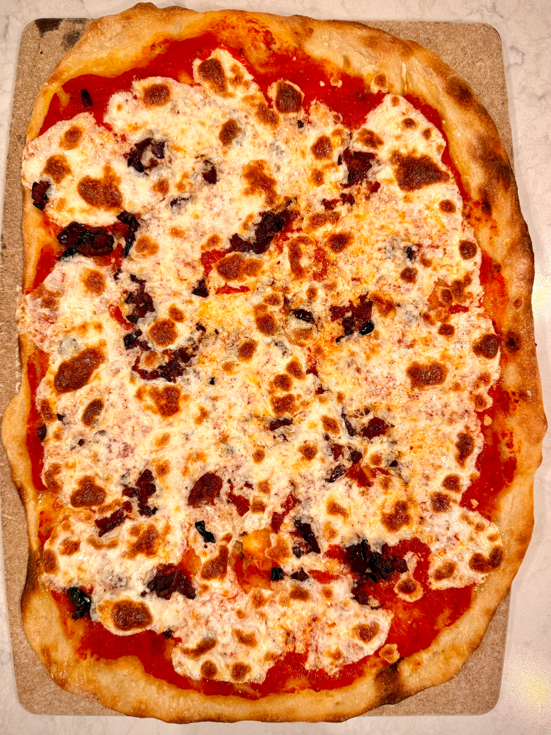 A rectangular pizza topped with melted cheese and a tomato sauce base is shown on a stone surface.