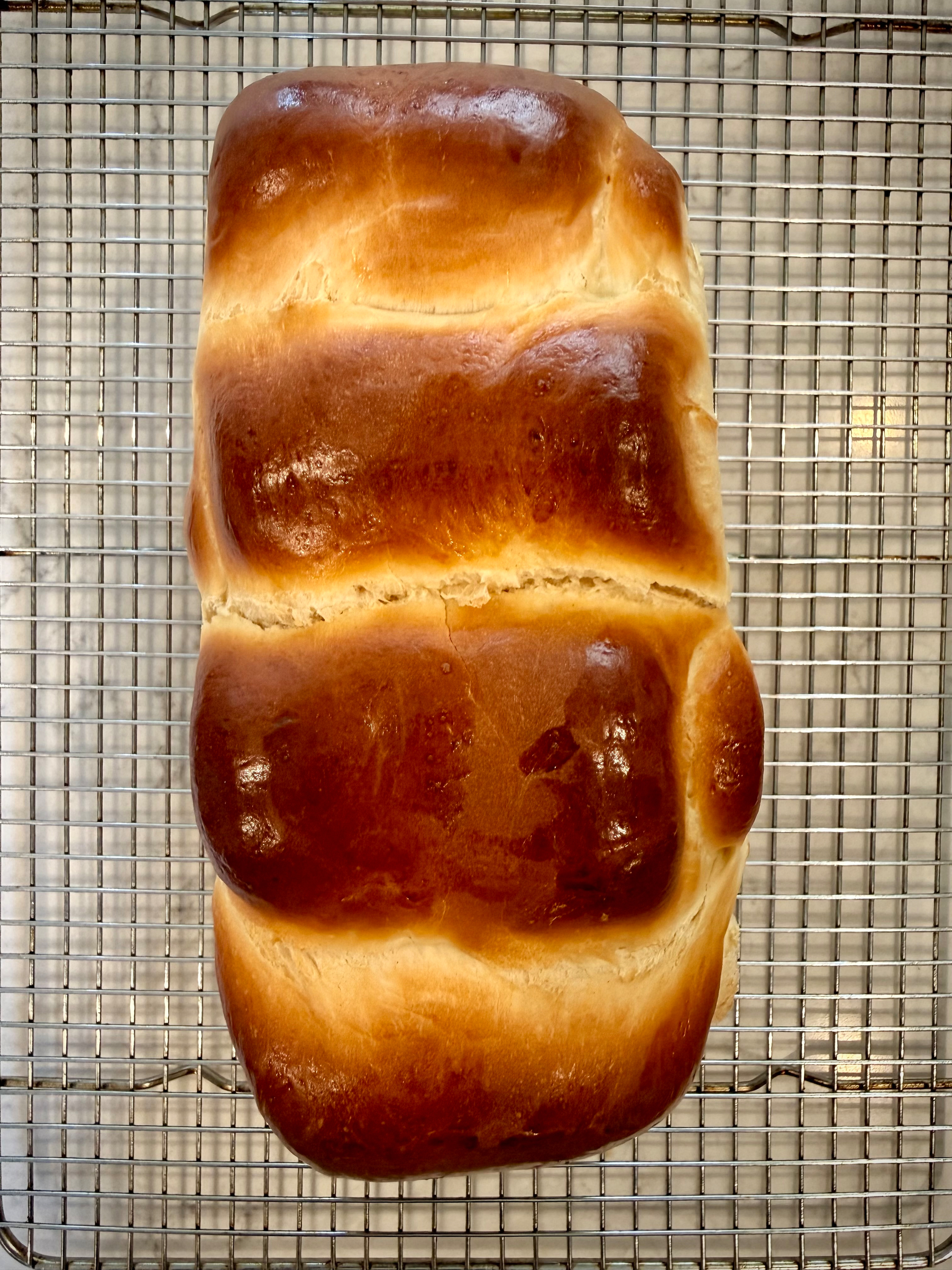 A loaf of golden-brown, freshly baked bread is resting on a cooling rack.