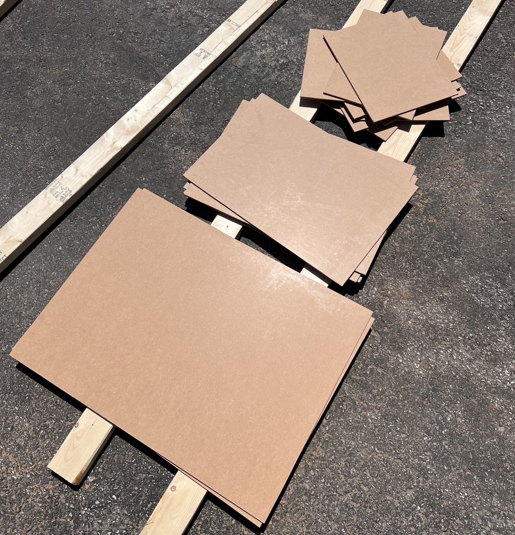 Fourteen pieces of hardboard cut up and lying in 3 piles on my driveway. 
