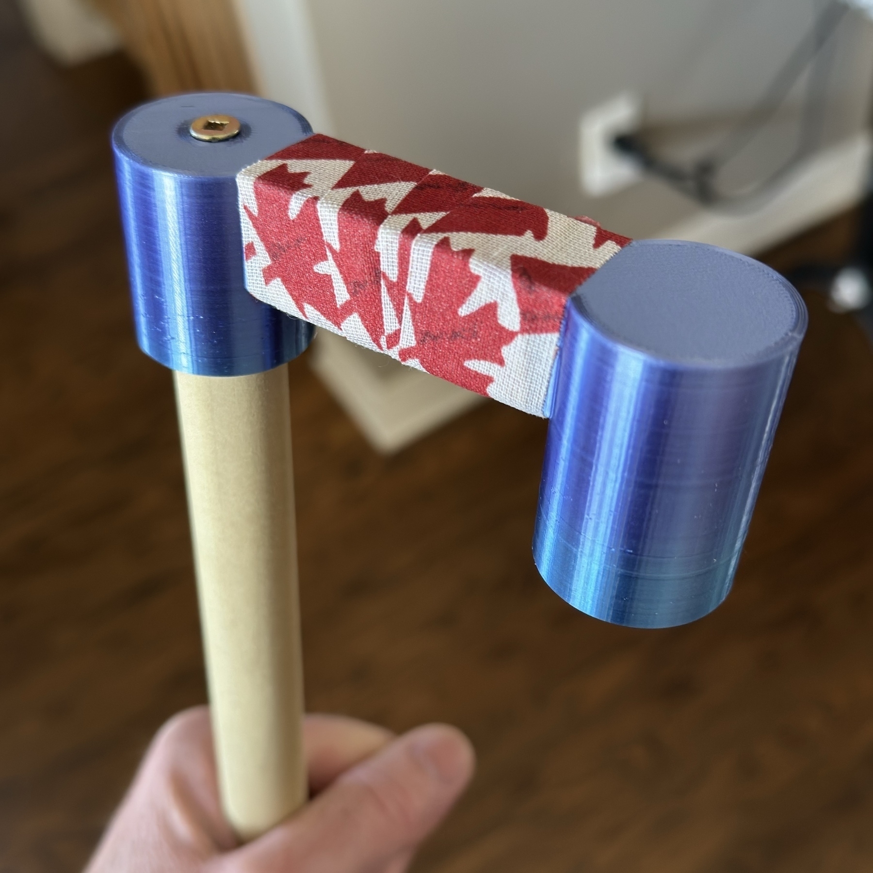 A 3D printed blue Mahl hook on the end of a piece of wood. Hockey tape with Canadian leaf is wrapped around the middle. 