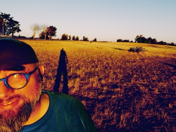 Photo of grassy field. I cast a long shadow, since the sun is low on the horizon.