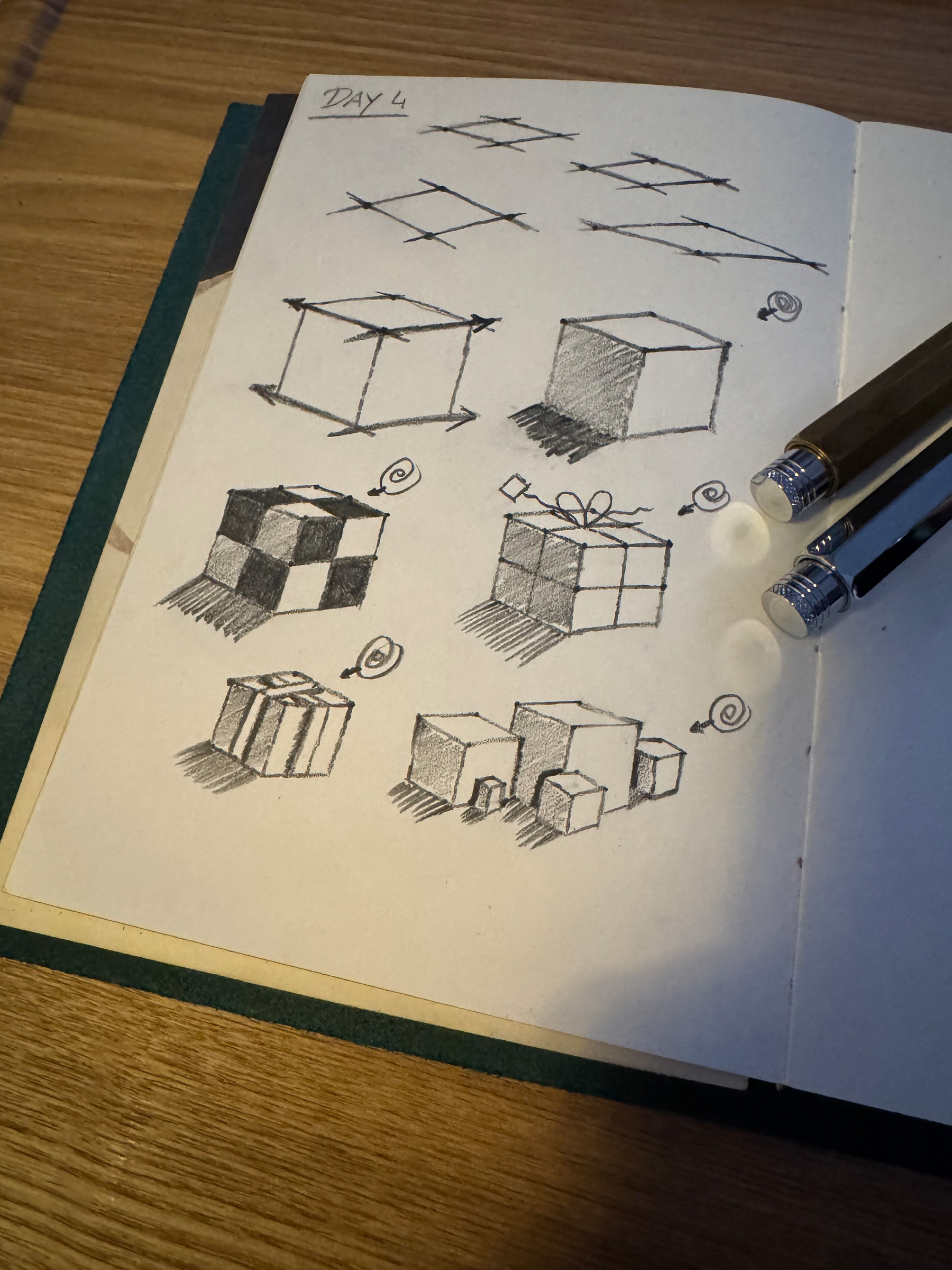 A sketchbook page features various pencil drawings of cubes with different patterns and shadows, accompanied by two pencils resting on the page.