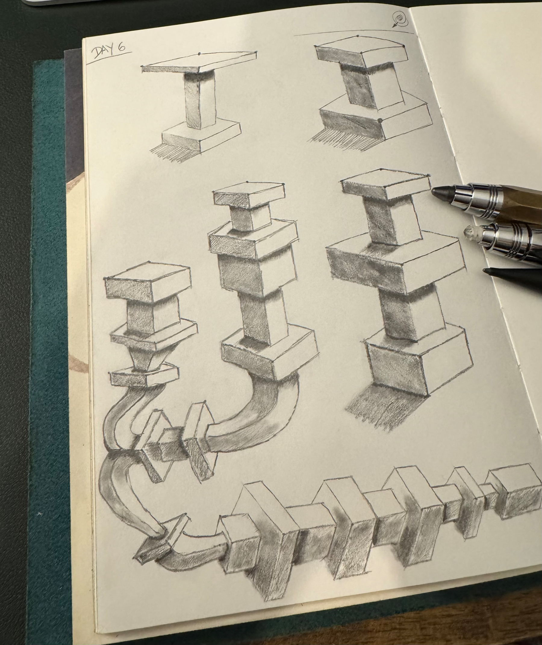 A sketchbook page features several drawings of abstract, geometric structures with interlocking rectangular shapes, alongside a pen.
