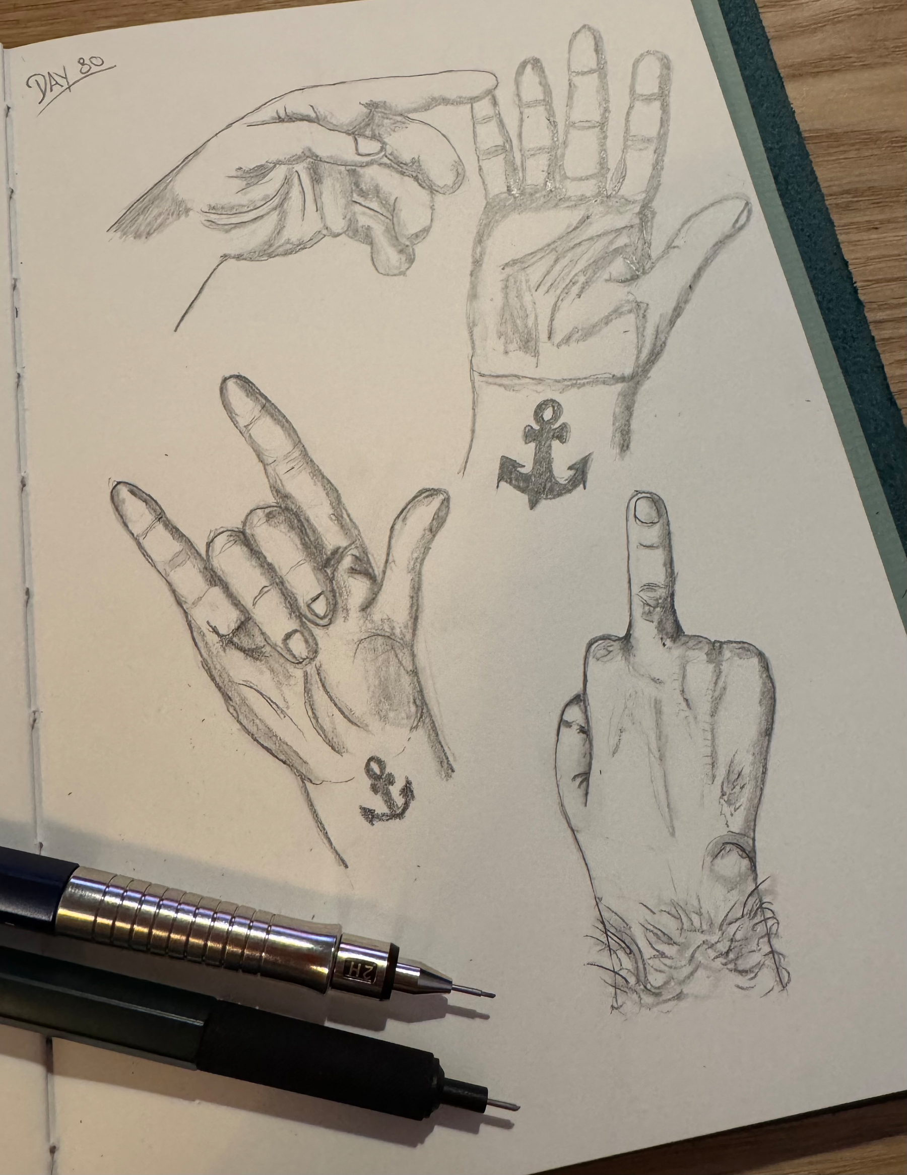 A sketchbook page features detailed pencil drawings of hands in various gestures, each with an anchor tattoo on the wrist, alongside two mechanical pencils.