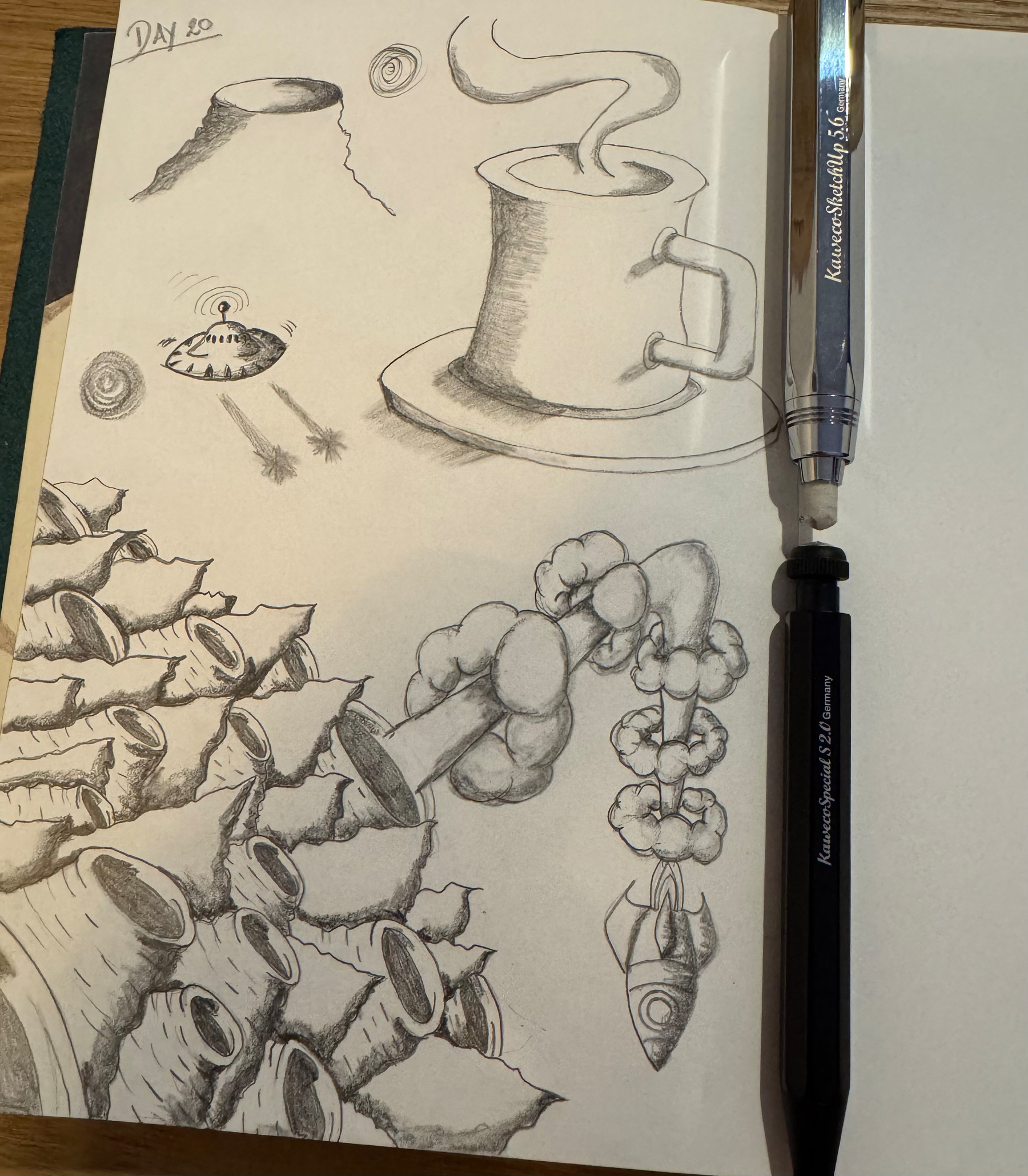 A sketchbook page features a steaming coffee cup, a flying saucer, a rocket, and a series of abstract, organic shapes, accompanied by two pens.