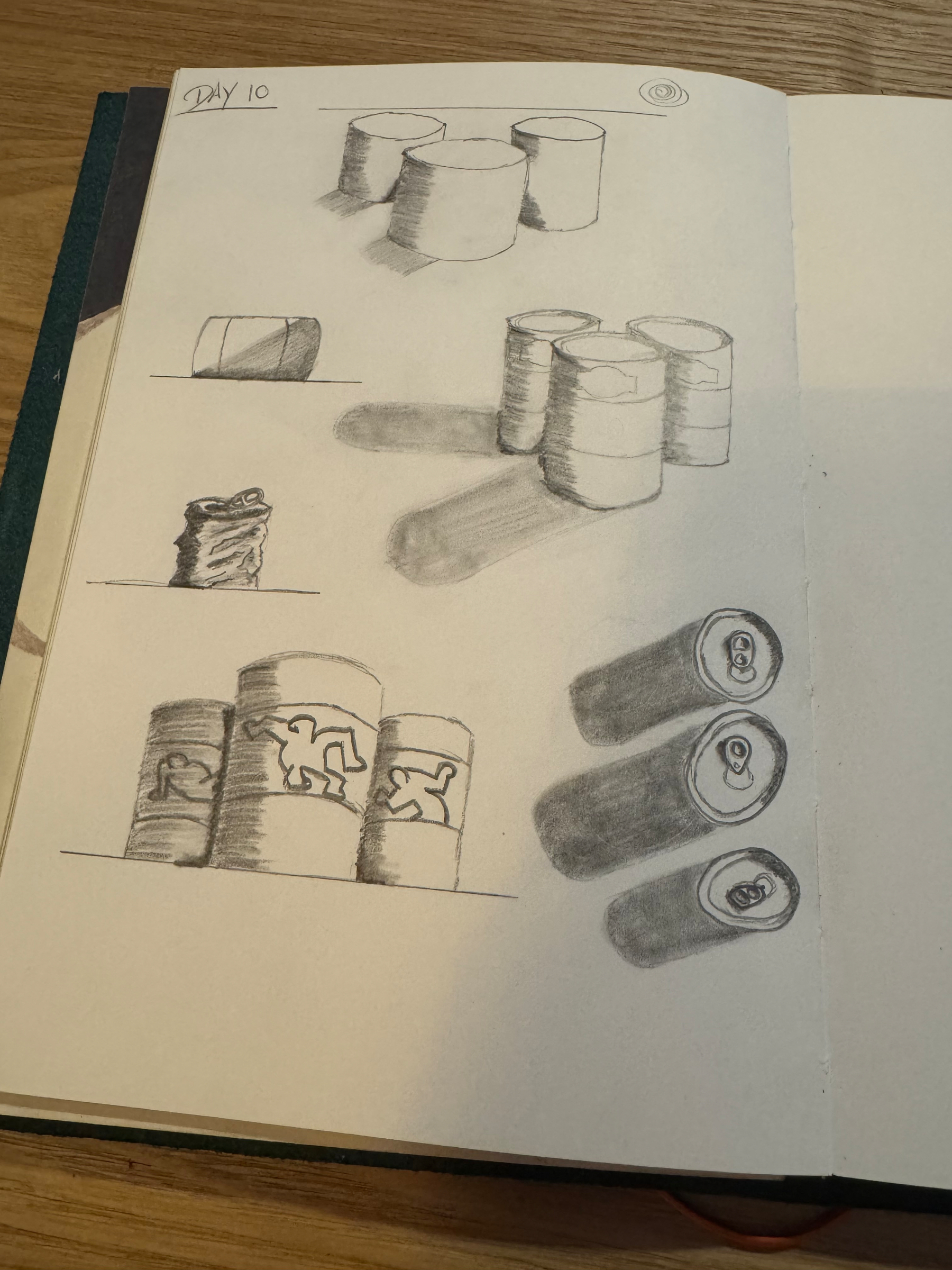 A sketchbook page depicts various shaded pencil drawings of cylindrical objects and cans.