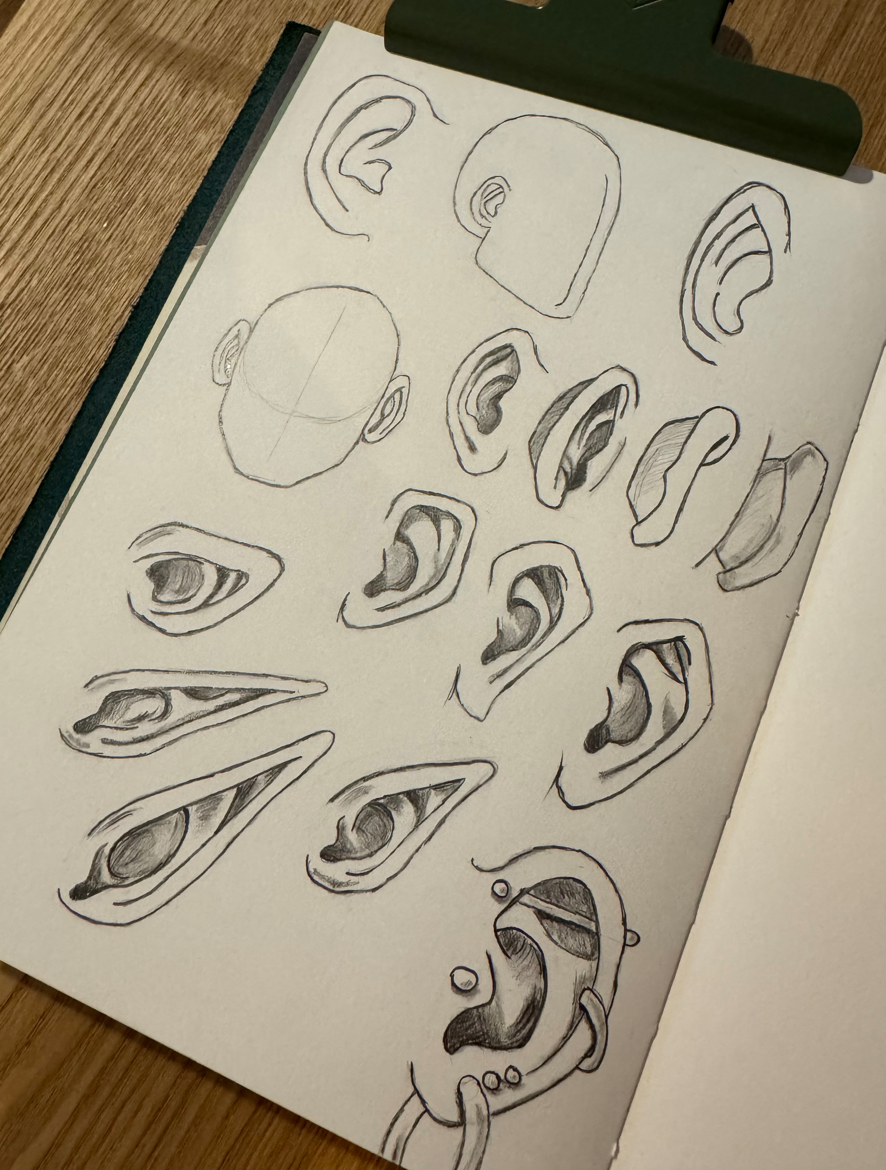 A sketchbook page displaying various pencil sketches of eyes, ears, and a partial face outline with a grid.