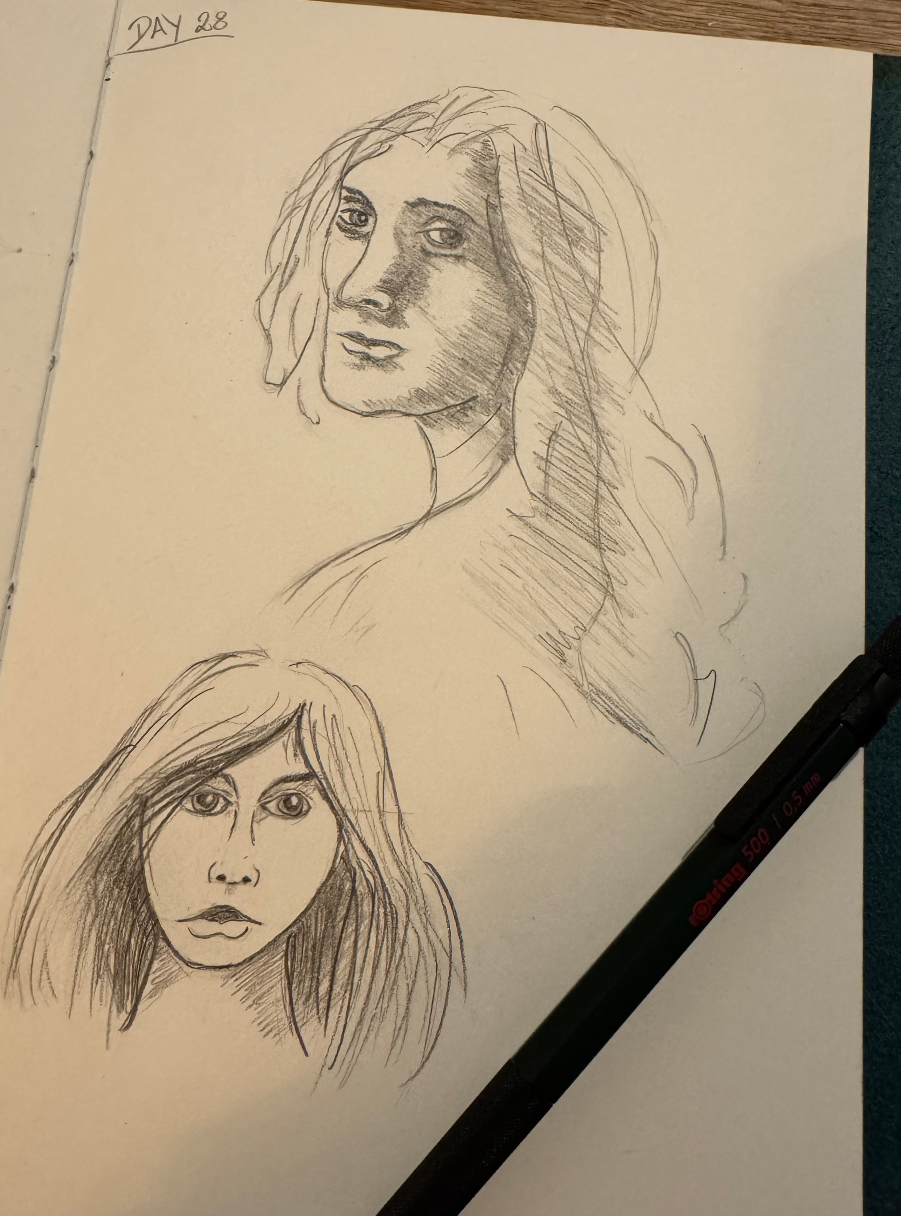 Two pencil sketches of faces are drawn on a page, accompanied by a black pencil.