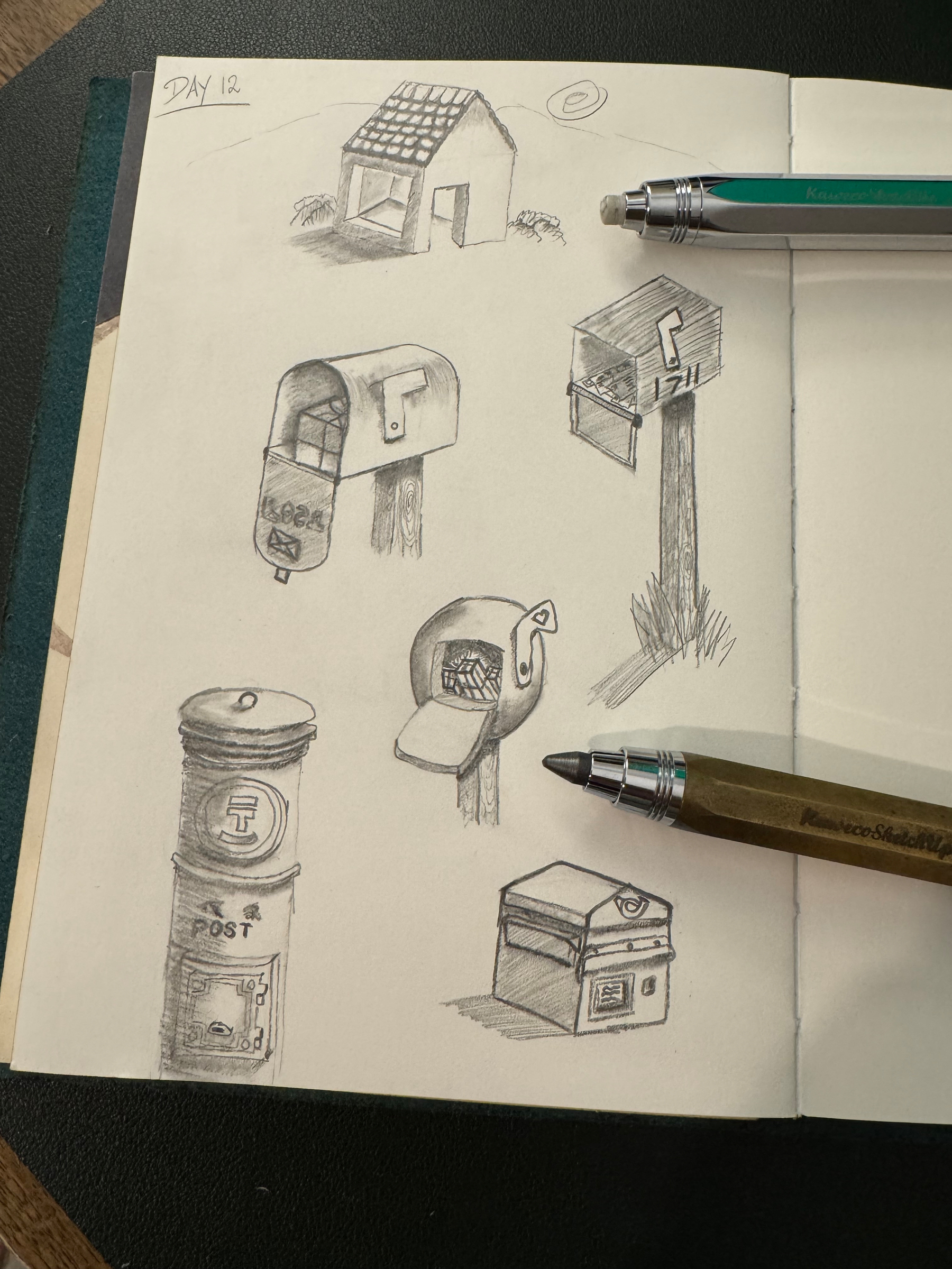 A sketchbook page displays various hand-drawn designs of mailboxes and a small structure, accompanied by two pens placed on top.