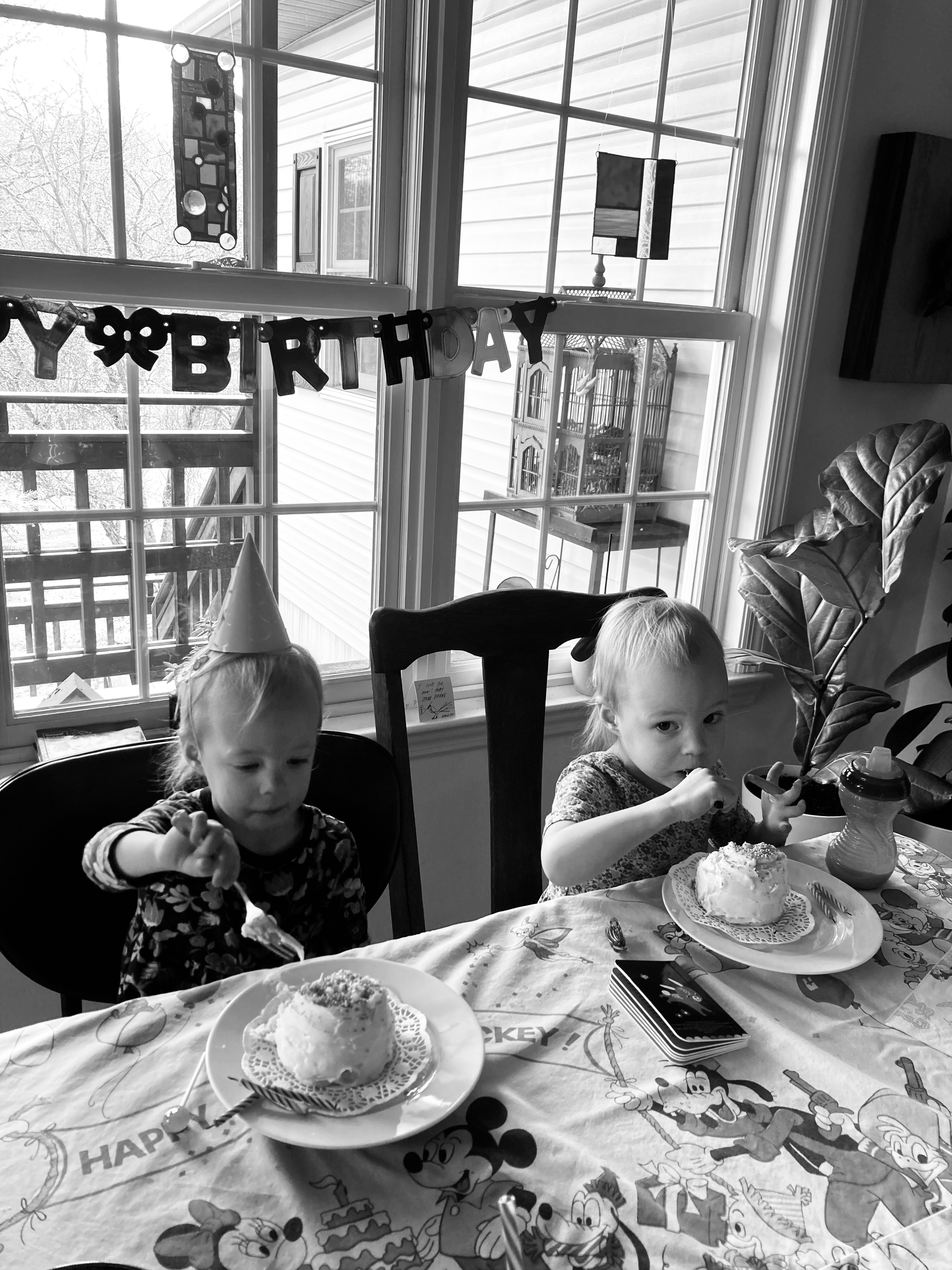 Black and white photo of twin girls eating cake at their third birthday party. 
