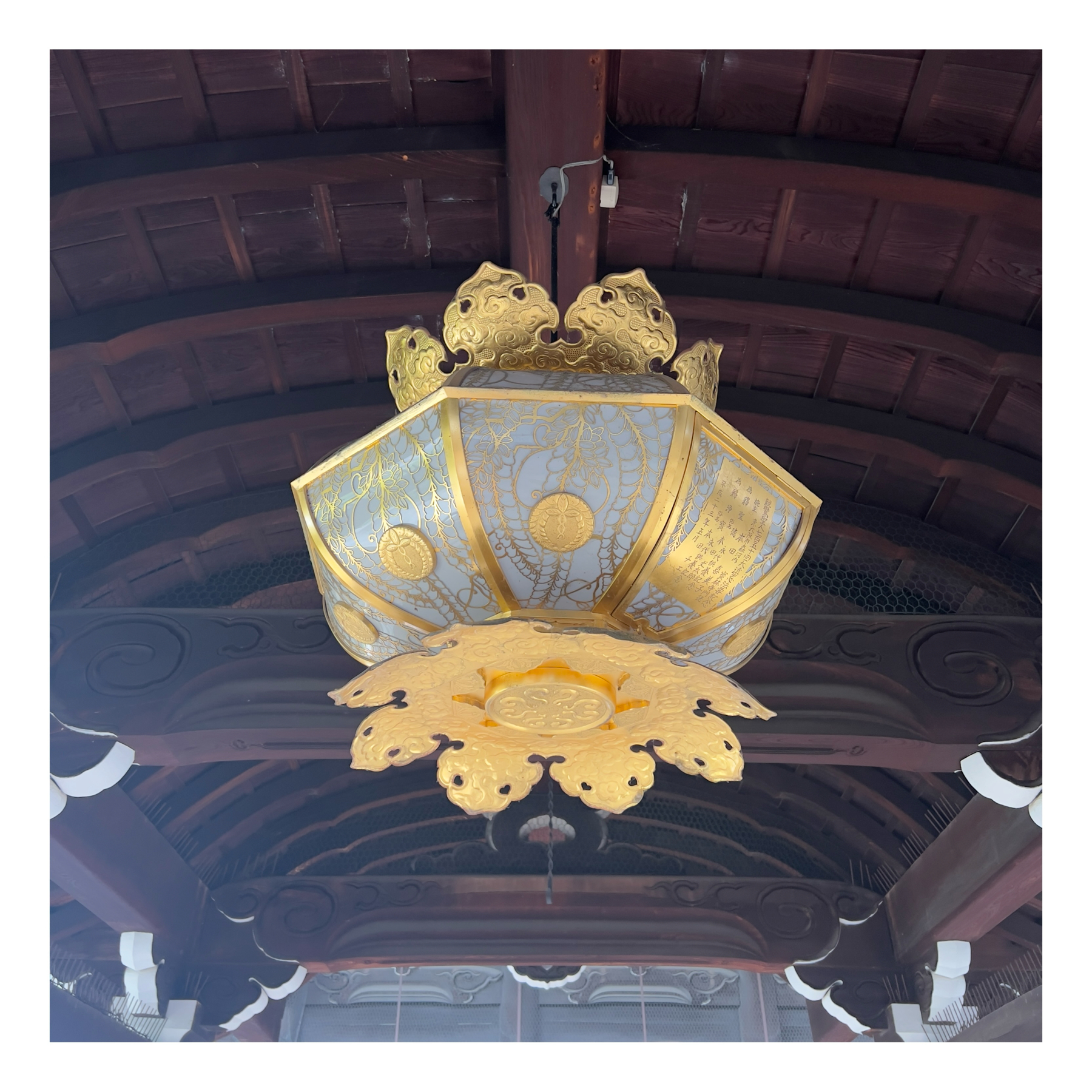 Ornate golden lantern hanging from a dark wooden ceiling with traditional detailing.