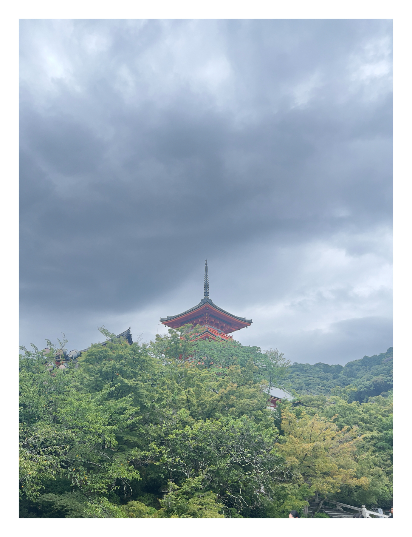 A pagoda peeks out amidst lush green foliage against a backdrop of gray, overcast skies.