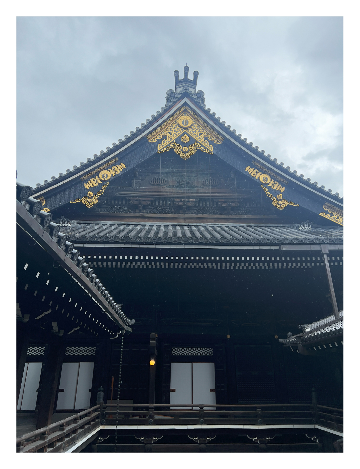 Traditional Japanese temple with intricate gold designs on the blue roof, wooden structure, and a hanging lantern, set against a hazy sky.