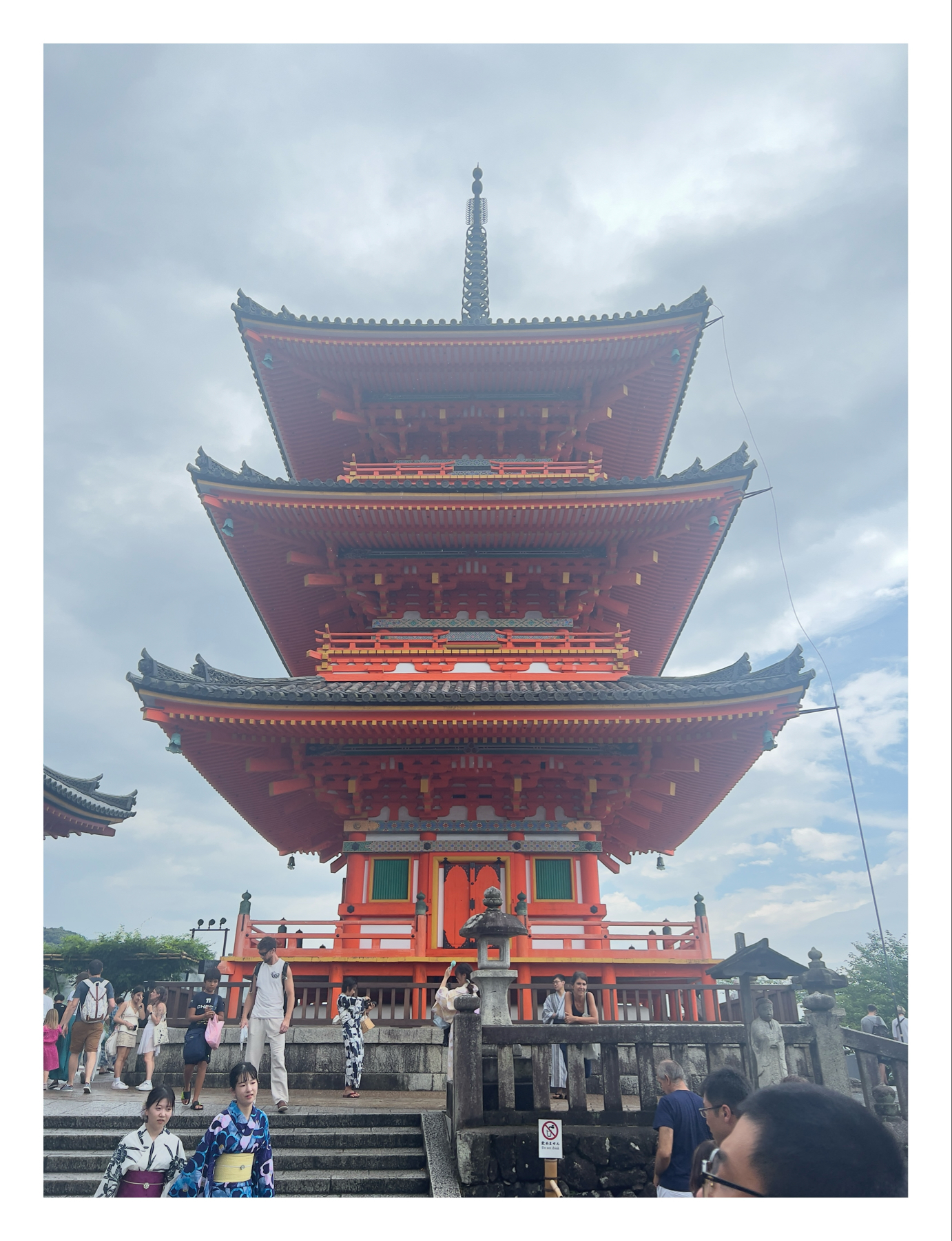 A vibrant red pagoda with multiple tiers surrounded by tourists, some wearing traditional Japanese attire, under a cloudy sky.