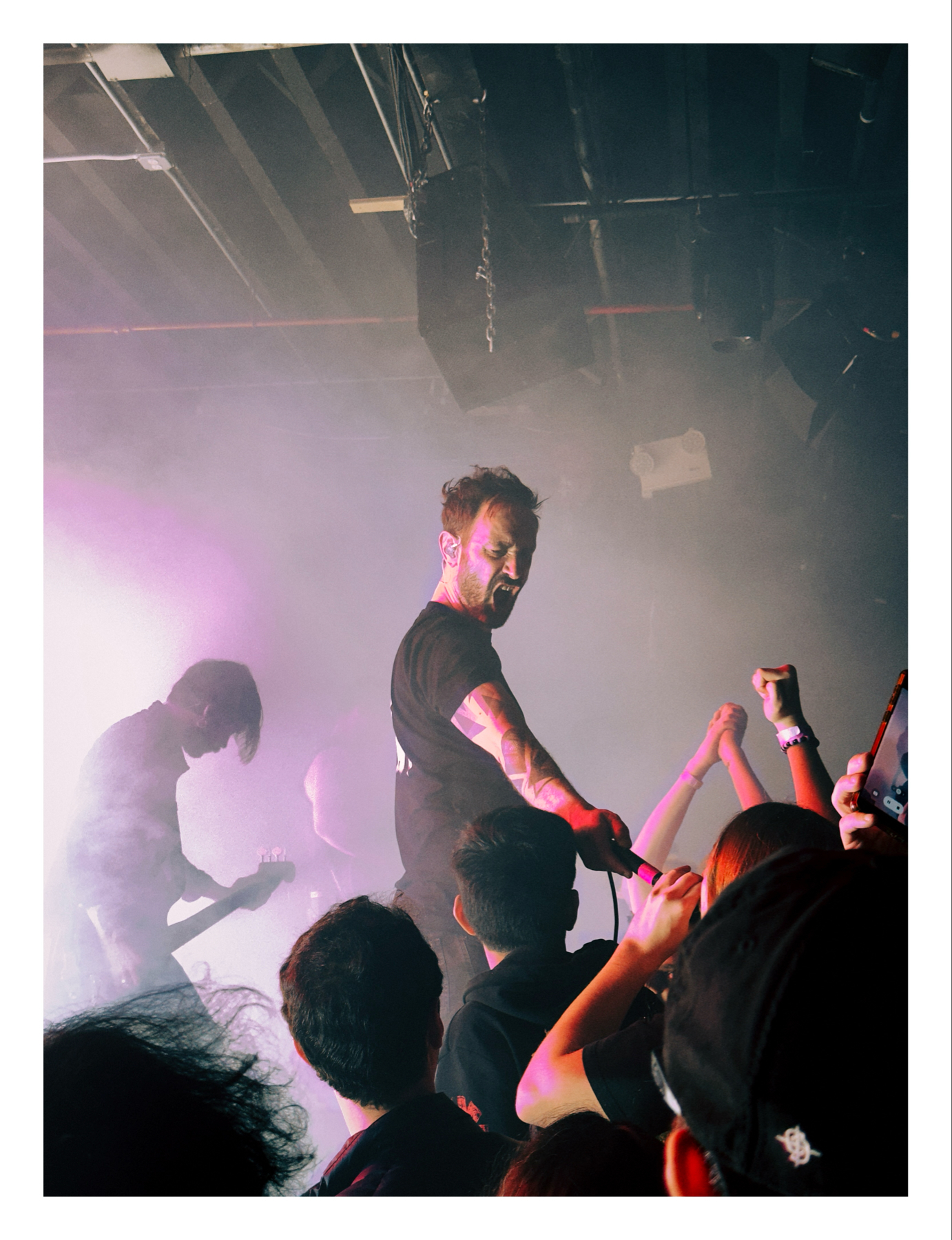 Live band performing on stage with vibrant purple lighting, engaging with an audience that is visible in the foreground.