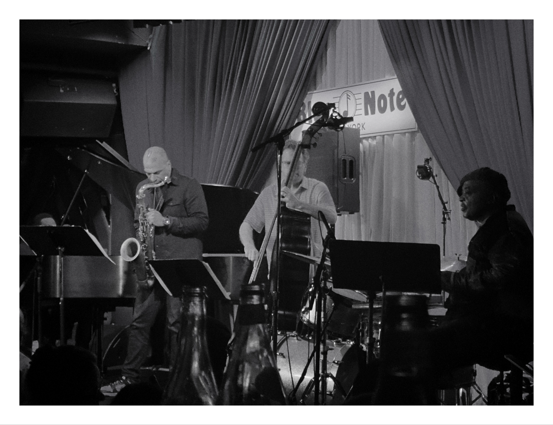 Black and white photo of a jazz trio performing at the Blue Note in New York, featuring a saxophonist, a pianist, and an upright bassist.