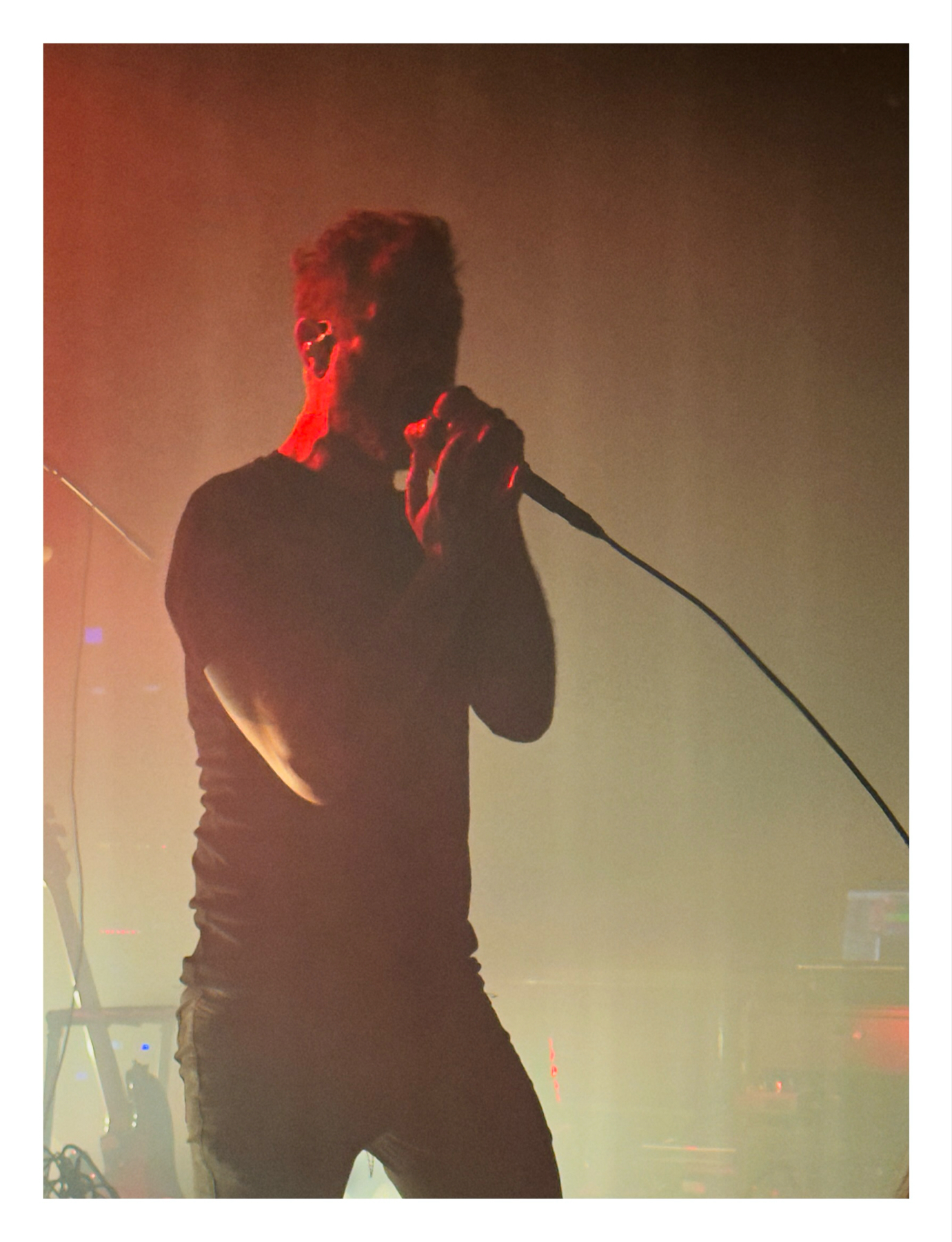 A silhouette of a musician singing into a microphone on stage with warm stage lighting in the background.