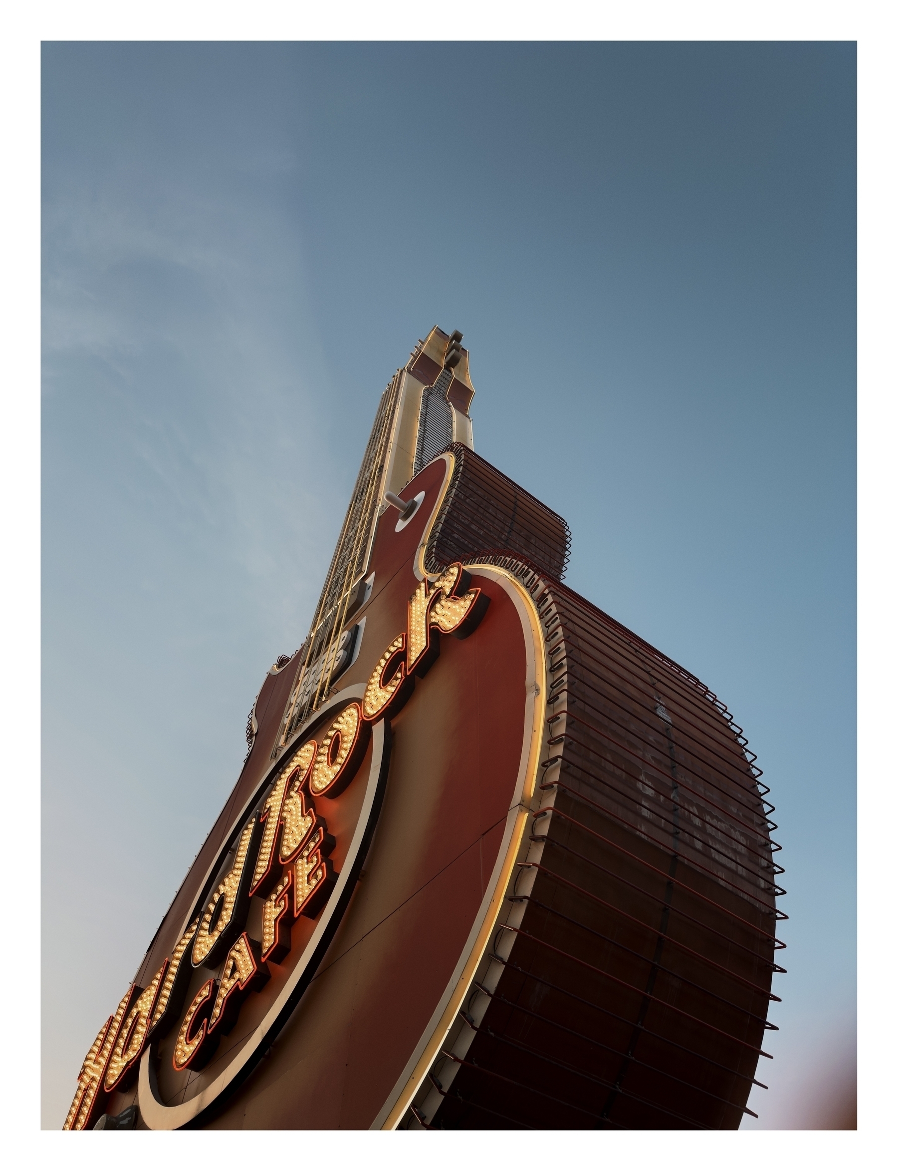 A towering, illuminated sign reads “Hard Rock Cafe,” set against a clear sky at twilight.