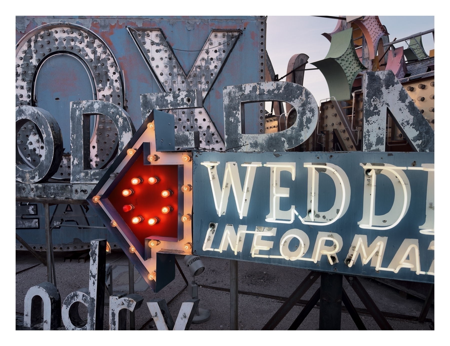 Weathered, oversized letters and illuminated signs, arranged haphazardly, create a vintage urban display set against a twilight sky.